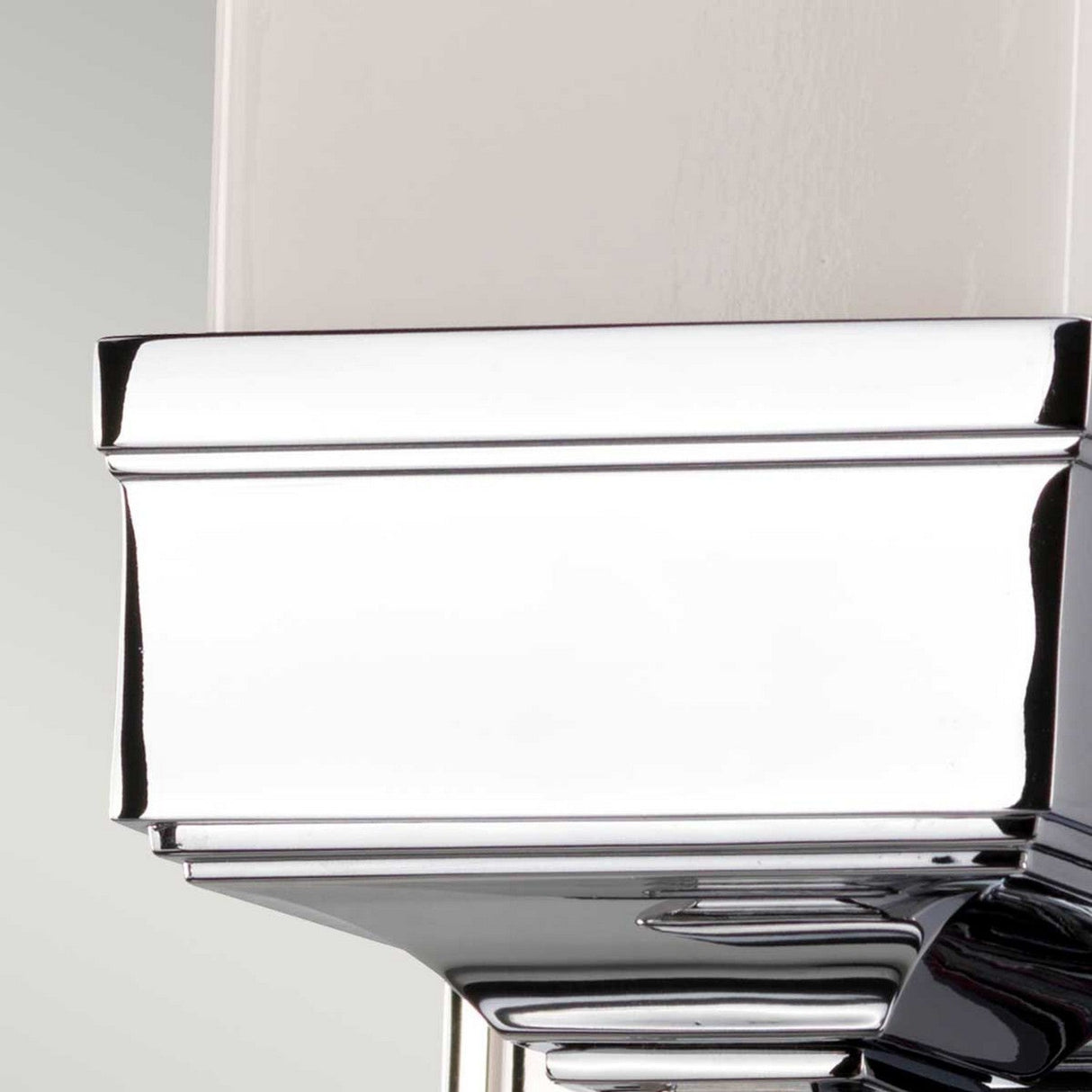 Close-up of the Cambridge Wall Light in polished chrome, showcasing smooth, angular surfaces that reflect surrounding light. Its gleaming chrome finish and clean lines lend a modern, sleek appearance, reminiscent of a sophisticated architectural detail.