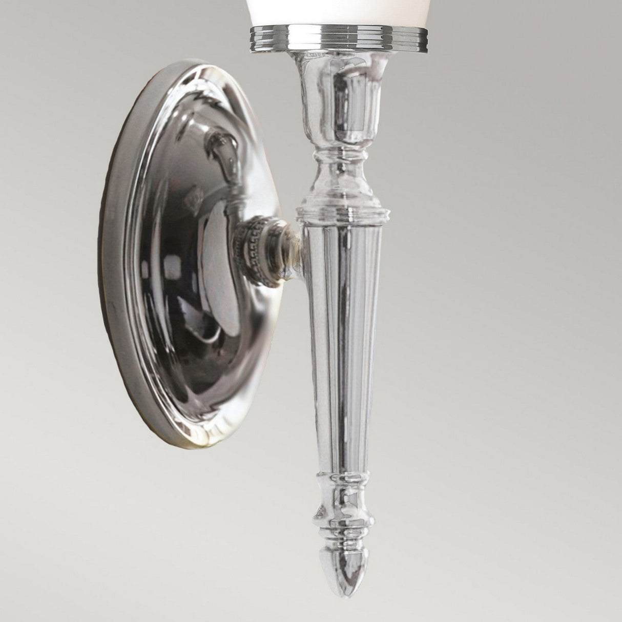 Introducing the Dryden-4 Wall Light in Polished Chrome: a wall sconce with sleek, polished chrome finish and intricate detailing. It boasts an elongated, tapered design featuring a white glass shade at the top, perfect against a neutral background for a sophisticated touch.