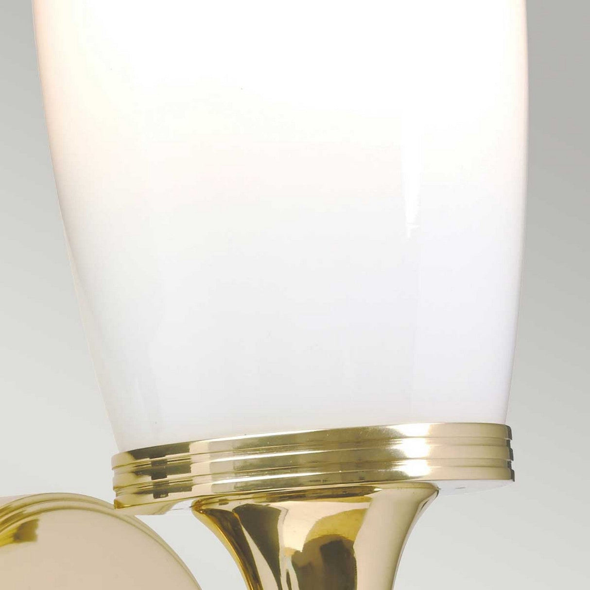 Close-up of the Eliot 1 Light Wall Light featuring a sleek design with a white shade and polished brass base. The glossy surface reflects light, highlighting its elegant style.