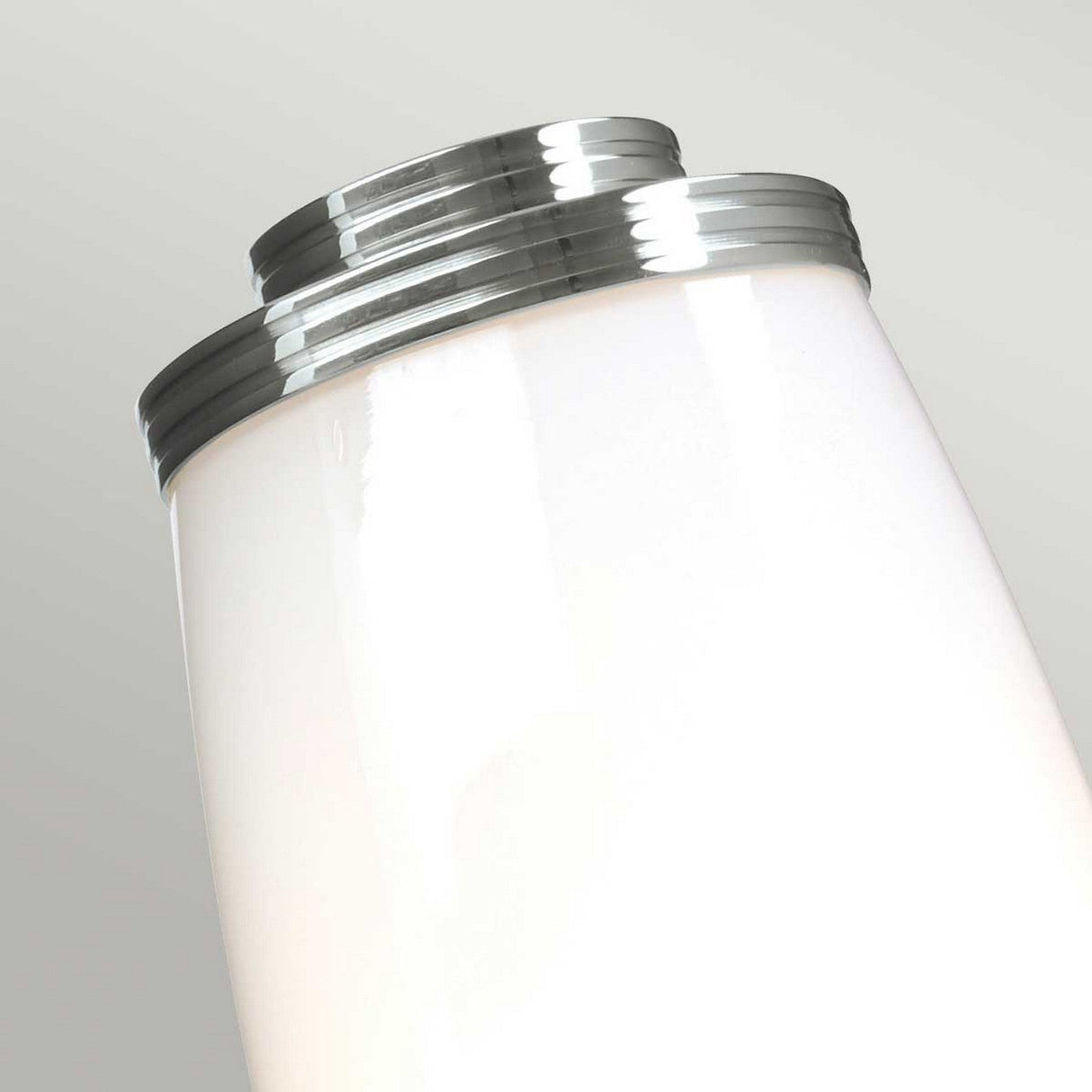 Close-up of the Eliot 1 Light Wall Light in polished chrome featuring a modern, cylindrical design on a light gray background. The lamp's sleek surface and metallic accents offer a minimalist and contemporary aesthetic, making it ideal for bathroom lighting with an LED G9 lamp for efficient illumination.