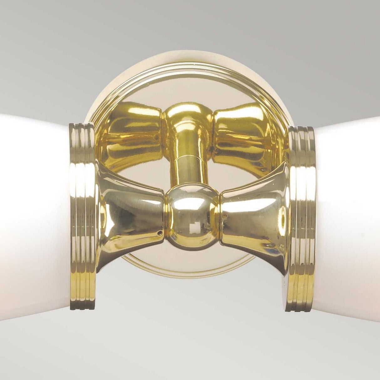 A close-up of the Eliot 2 Light Wall Light - Polished Brass reveals its polished finish with two frosted glass shades extending from each side. This fixture showcases a reflective surface and decorative ridges, set against a plain background, perfectly exemplifying elegant LED bathroom lighting with an IP44 rating for enhanced durability.