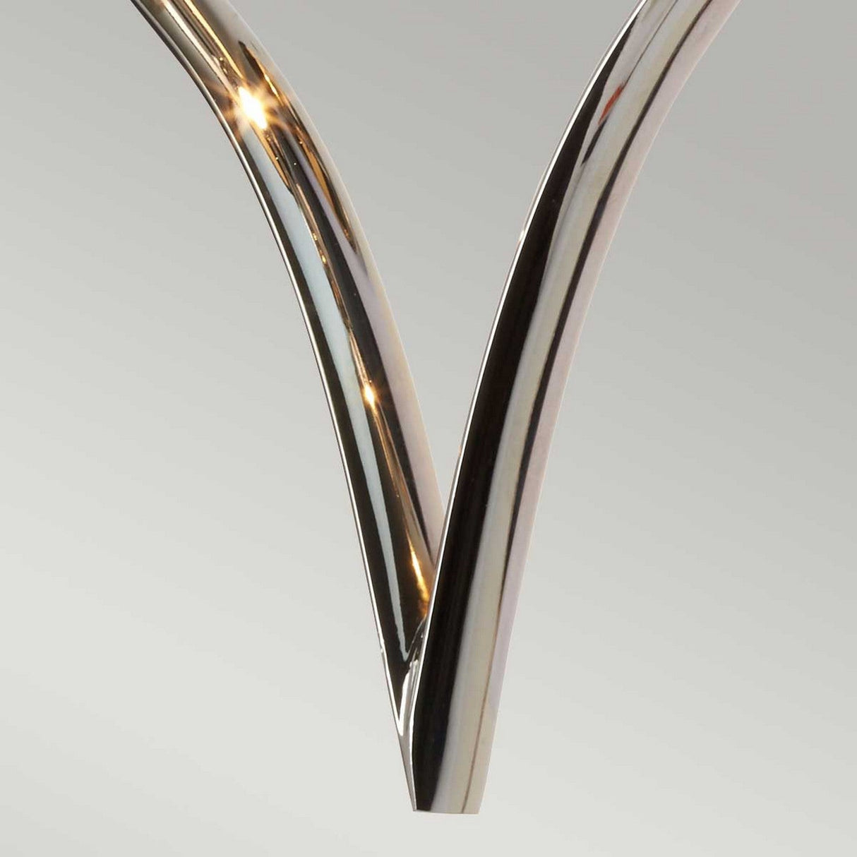 Close-up of a metallic, V-shaped sculpture featuring smooth, polished chrome surfaces that gleam as they catch the light. The backdrop is a gentle, neutral hue that highlights the sculpture's sleek and contemporary design, evoking the aesthetic of a Falmouth Wall Light - Polished Chrome/Black Shade.