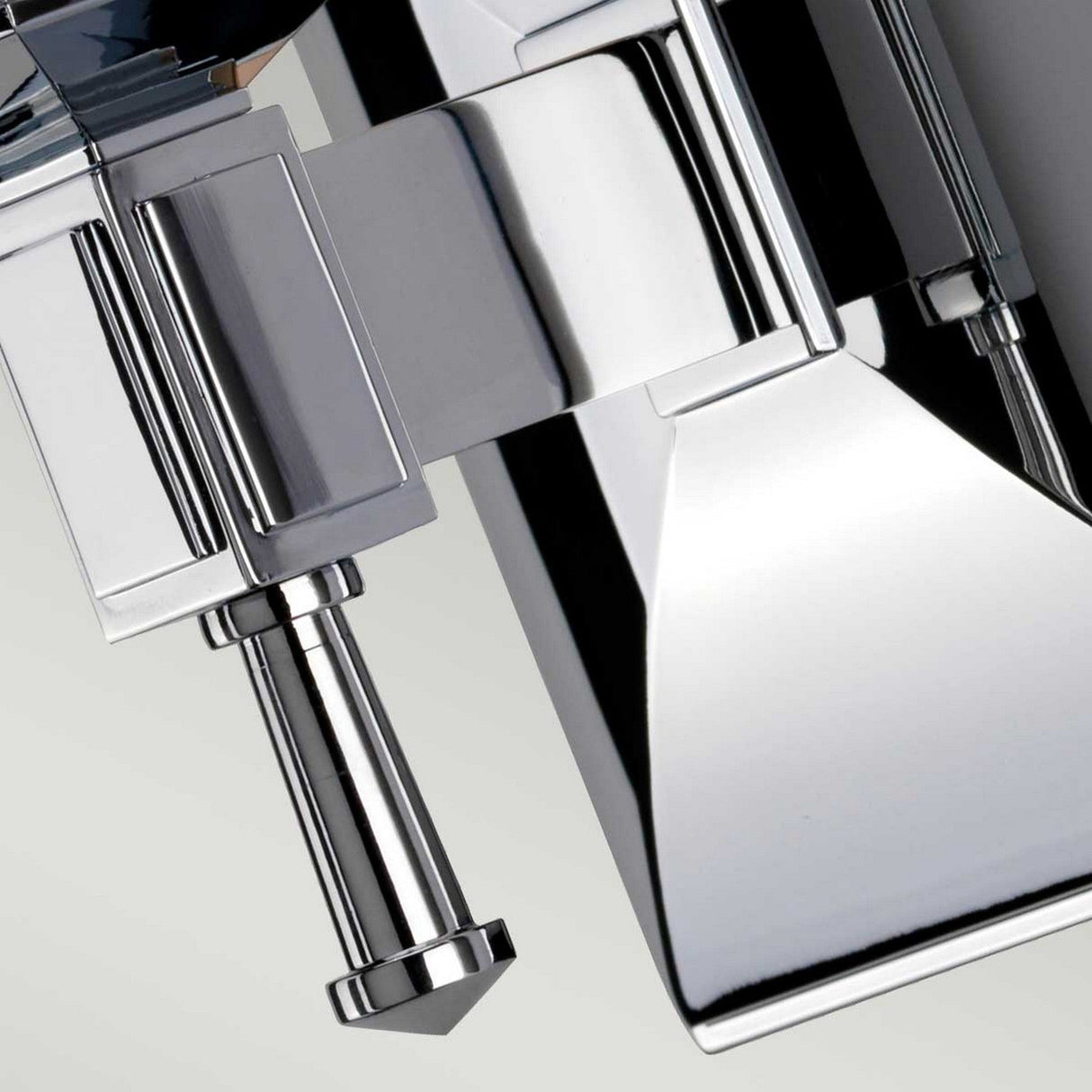 Close-up of a shiny, polished chrome mechanical part with a geometric design. Featuring a cylindrical protrusion and angular surfaces, it gleams like the Shirebrook 1 Light Wall Light - Polished Chrome, reflecting light off its polished finish.