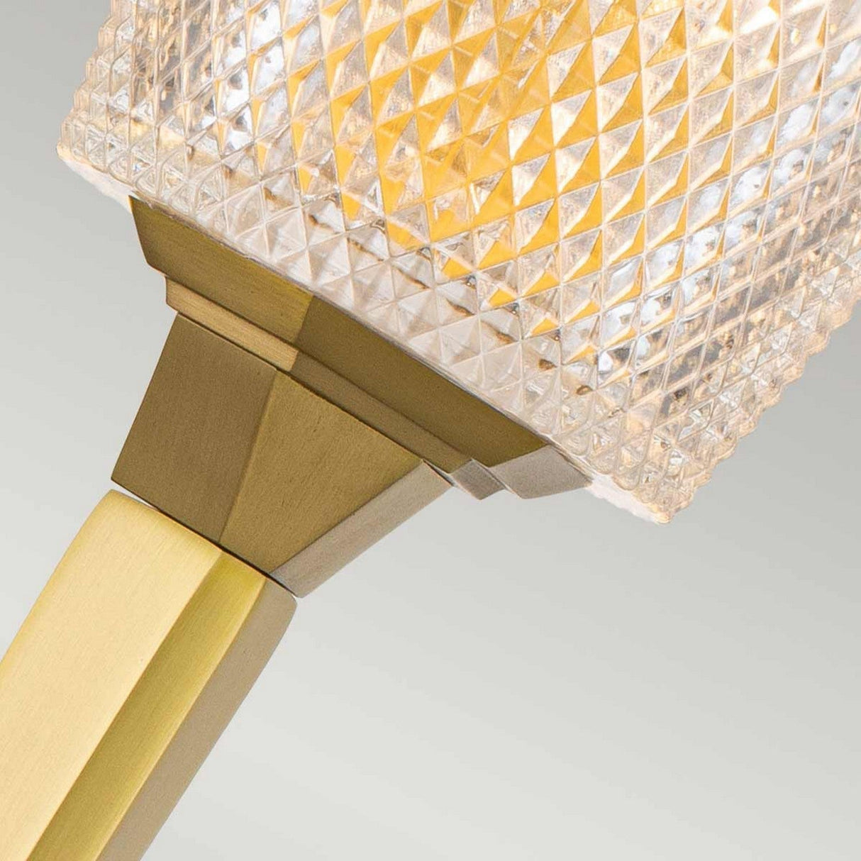 Here is a close-up of the Verity 1 Light Wall Light, showcasing its elegant cut glass shade that emits a warm glow. This energy-efficient LED light features a brushed brass base and sleek, modern design, seamlessly complementing the neutral background.