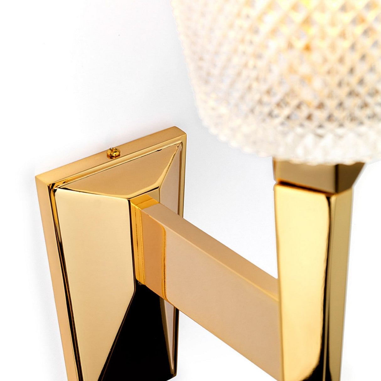 A close-up of the Verity 1 Light Wall Light reveals its luxurious design, featuring a modern gold metallic base and a textured glass lampshade. This elegant lamp is mounted on a rectangular polished gold fixture and incorporates energy-saving LED technology to enhance its sophisticated glow.