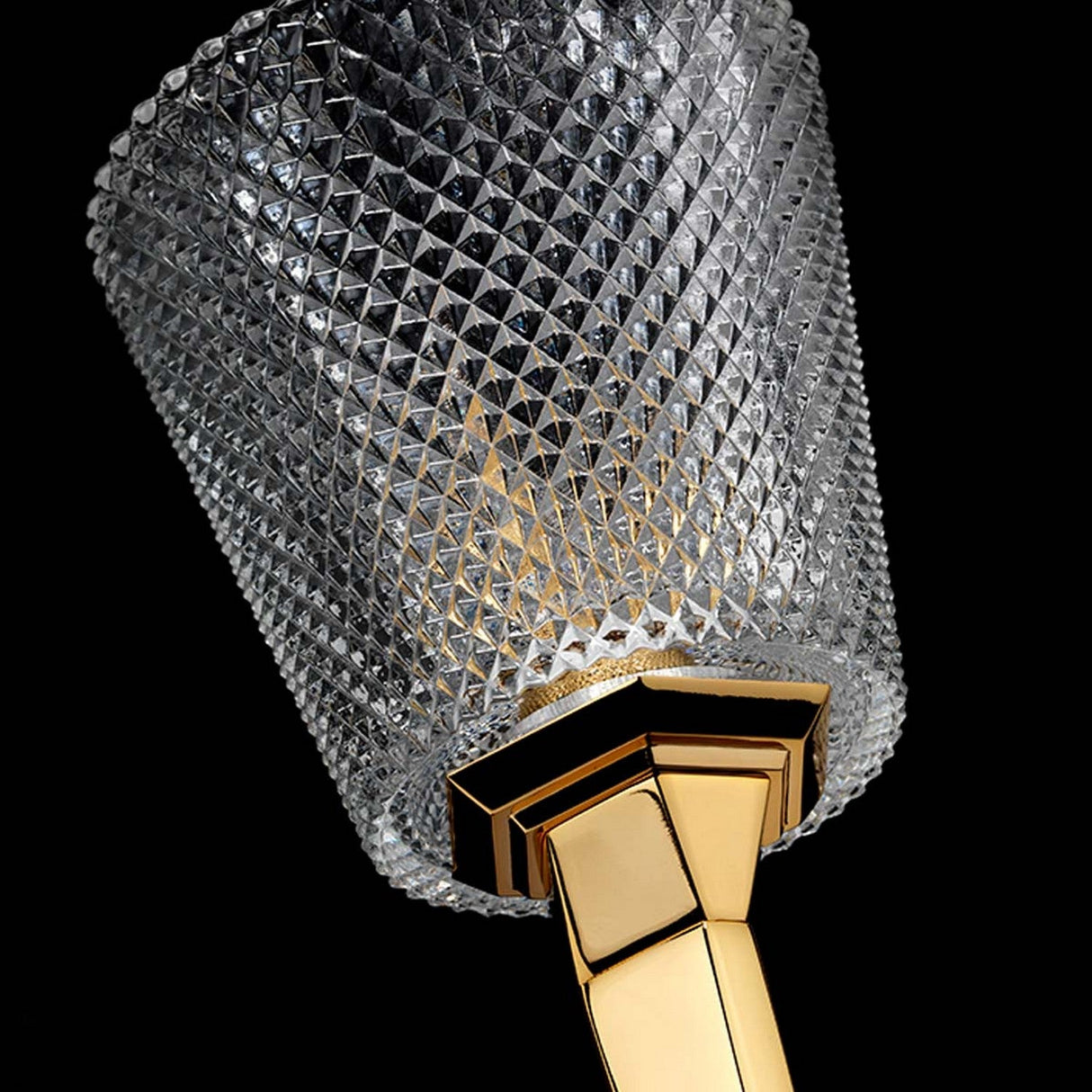 A close-up showcases the luxurious Verity 1 Light Wall Light, featuring a crystal glass fixture with a diamond pattern set against a black background. Its elegant design is accentuated by the sleek, polished gold base.