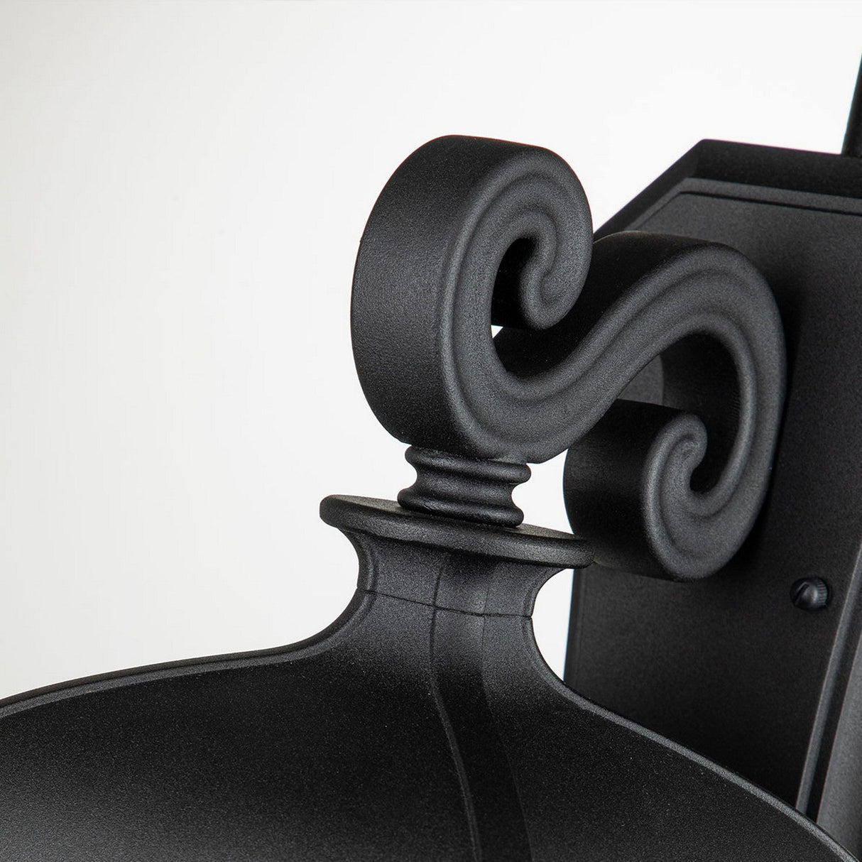 Close-up of the Bayview 1 Light Outdoor Large Wall Lantern in black, featuring a scrollwork bracket. The Georgian-inspired design showcases intricate curves and a matte finish, seamlessly enhancing outdoor spaces with an elegant touch against a light background.