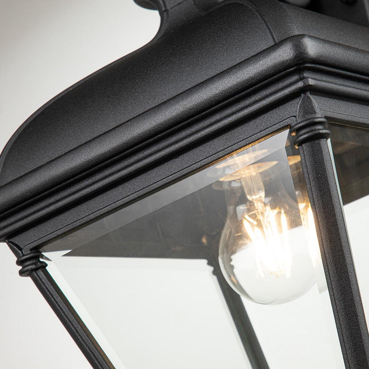 Close-up of the Bayview 1 Light Outdoor Large Wall Lantern in black, featuring a clear glass enclosure that reveals a glowing filament bulb inside. This large wall light showcases a Georgian-inspired design with decorative detailing at the corners, making it an ideal addition for enhancing outdoor spaces.