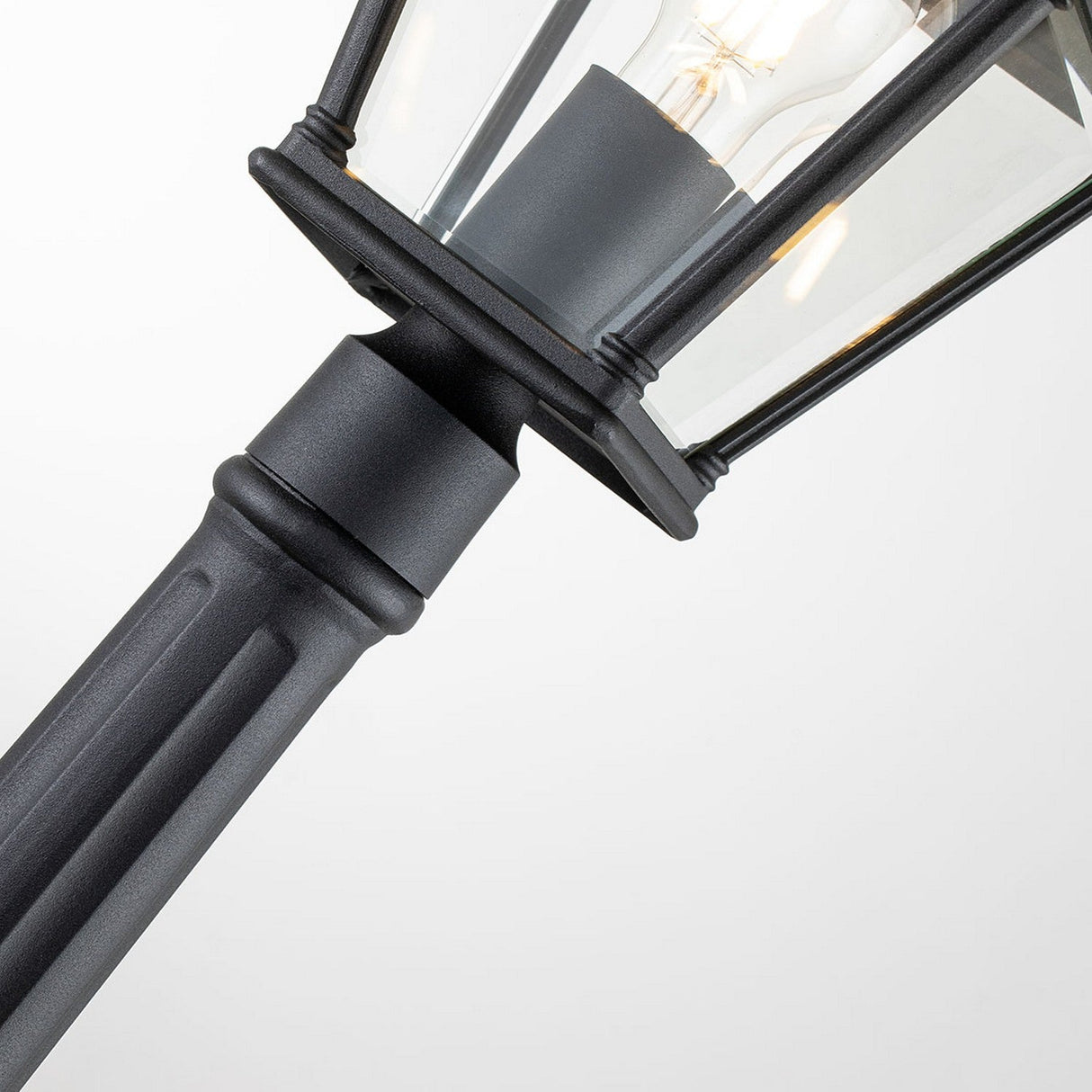 Close-up of the Bayview 1 Light Medium Pillar Lantern - Black, showcasing a lantern-style light fixture with clear glass that embodies Georgian-inspired elegance. The visible bulb inside casts a glow that enhances the pillar lantern's charm against the plain white background.