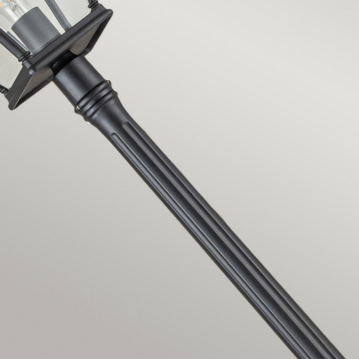 A close-up of the Bayview 1 Light Lamp Post in black highlights its classic design, featuring a lantern-style top and clear glass panels. The image captures the sleek, vertical lines and detailed ridges of the pole, embodying timeless outdoor lighting against a light gray background.