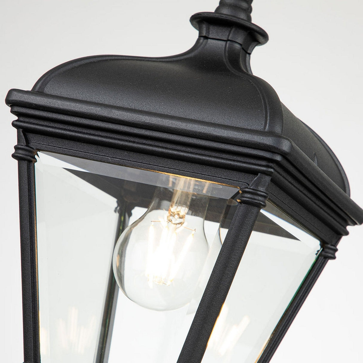 Here's a close-up view of the Bayview 1 Light Outdoor Medium Chain Pendant in black, featuring clear glass panels that reveal an exposed light bulb inside. This hanging chain pendant exudes Georgian elegance with its traditional design and decorative top, infusing outdoor spaces with timeless charm.