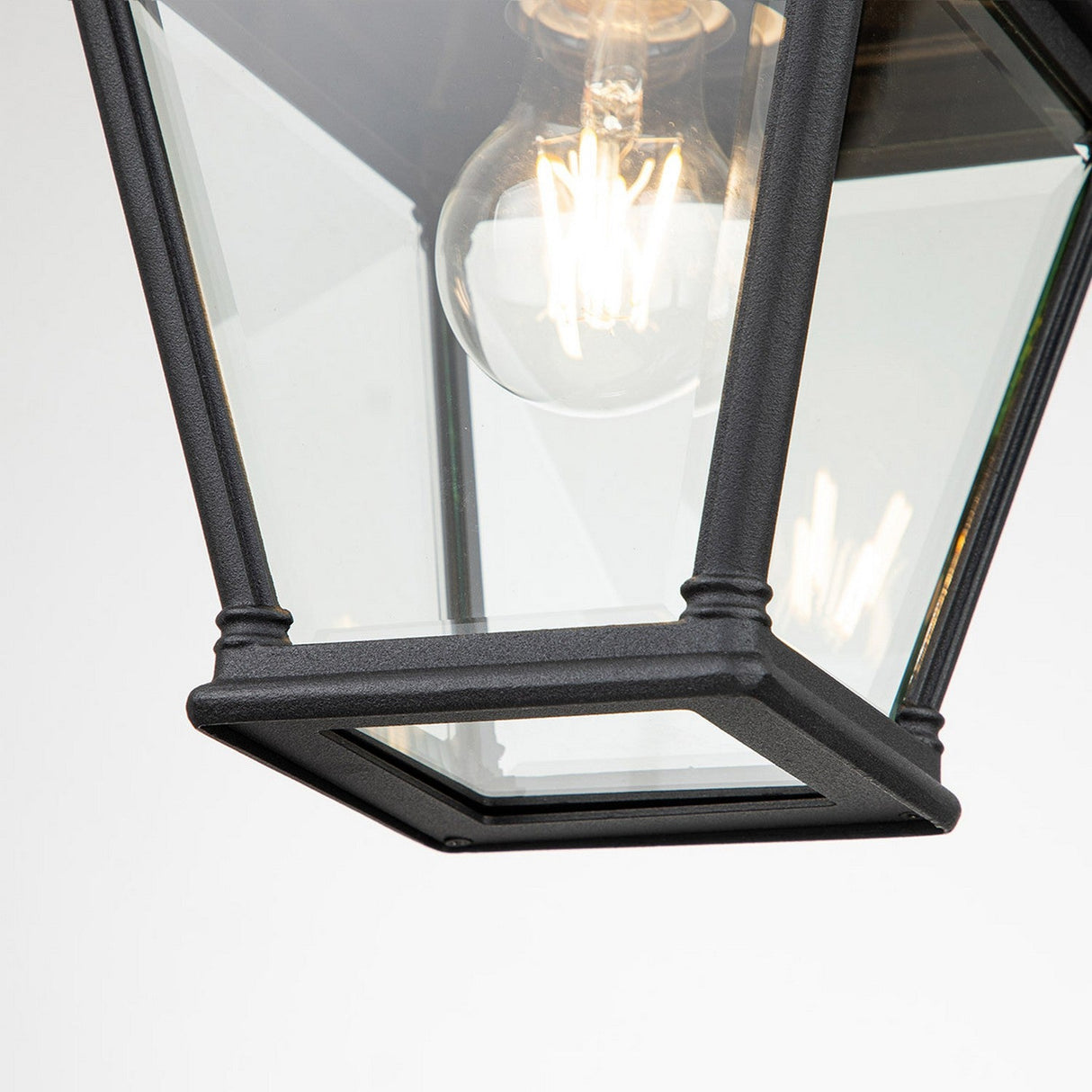 Close-up of the Bayview 1 Light Outdoor Medium Chain Pendant in black, featuring clear glass panels that exude Georgian elegance. A glowing light bulb with visible filaments is centered inside. The pendant, ideal for outdoor lighting, is set against a white background, emphasizing its classic, angular design.