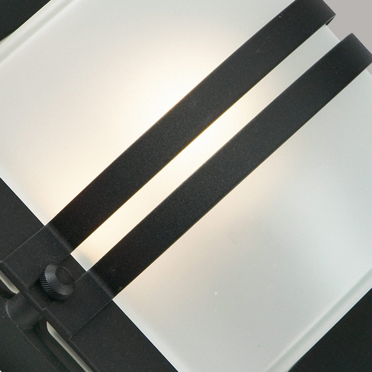 Close-up of the Bern Outdoor 1 Light Wall Lantern - Black With Frosted Glass featuring two parallel black metal bars. The light shines softly through the frosted glass, creating a warm ambiance reminiscent of Art Deco lighting.
