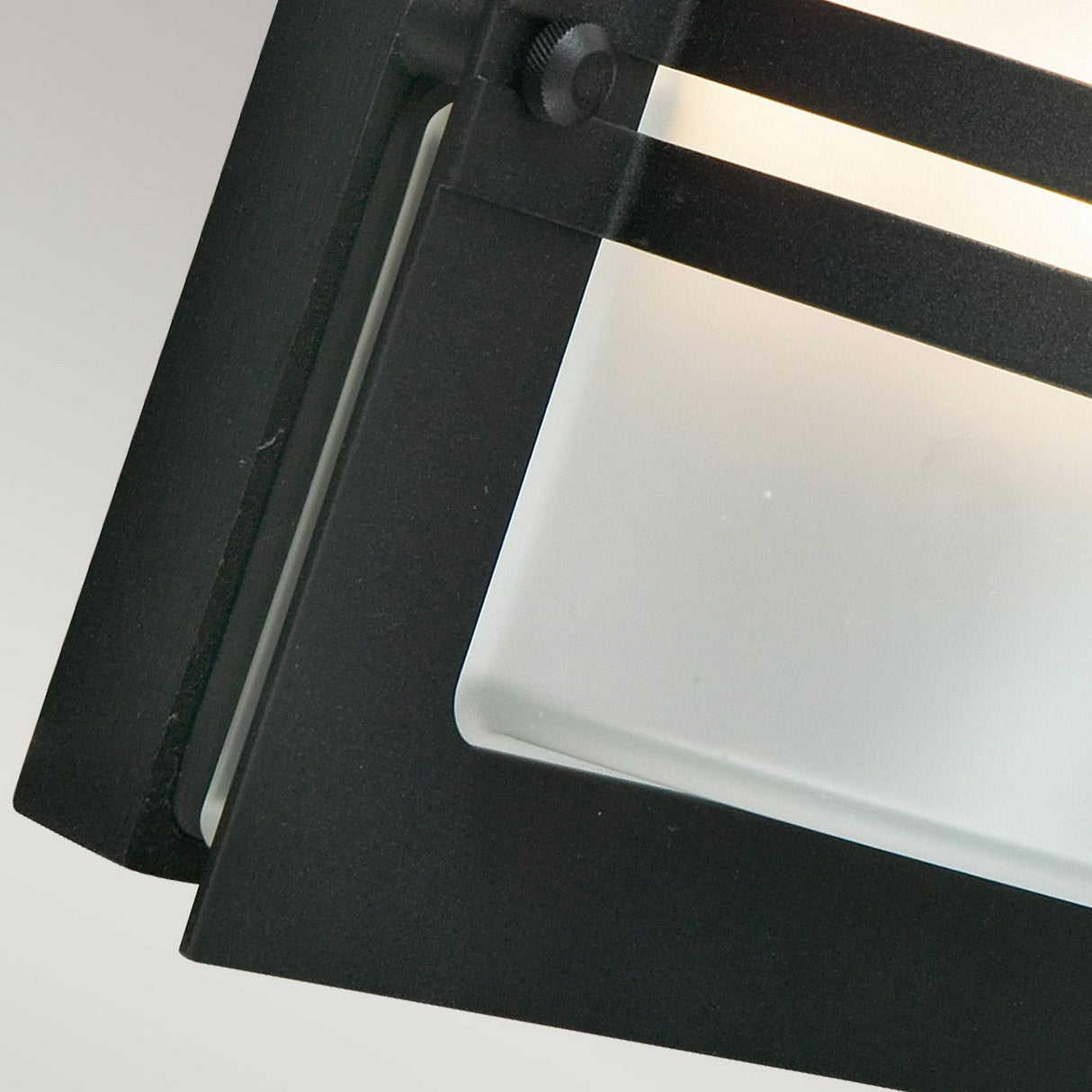 Close-up of the Bern Outdoor 1 Light Wall Lantern, featuring a black metal frame and a frosted glass panel, gently lit.