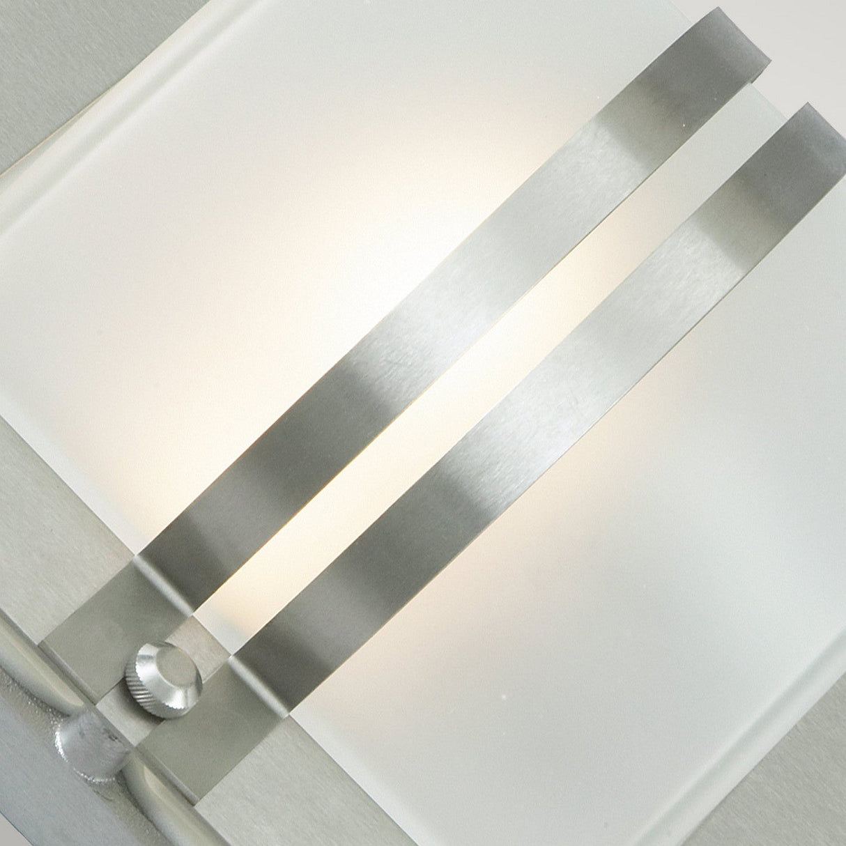 The Bern Outdoor 1 Light Wall Lantern, crafted from stainless steel with frosted glass, resembles a modern frosted glass lantern. It features two parallel metal strips that cast soft white light against the frosted panel. Its sleek and minimalist design includes a small circular knob at the base, making it perfect for contemporary interiors.