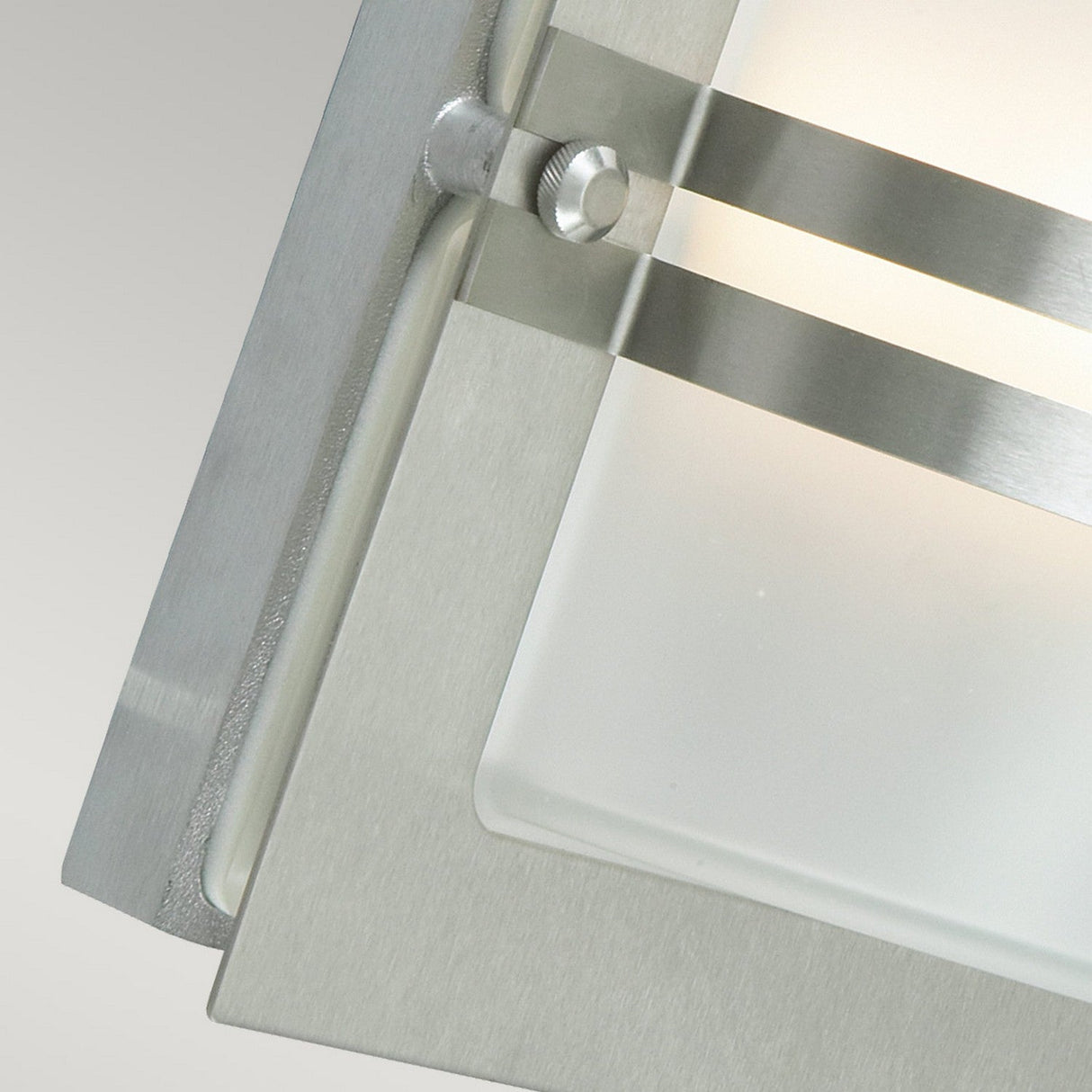 Close-up of the Bern Outdoor 1 Light Wall Lantern in stainless steel, showcasing its frosted glass panel framed by brushed metal and adorned with horizontal metal bands. The sleek and contemporary design emphasizes the lantern's minimalist aesthetic.