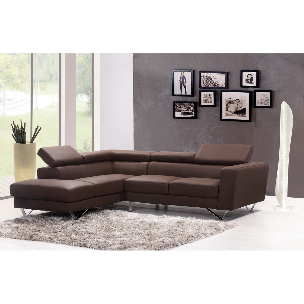 A modern living room with a brown sectional on a gray rug, decorative floor vase, and sculptural lighting from the Bianca LED Floor Lamp 30W 3000K - White. A gray accent wall displays framed photos, and large windows reveal lush greenery outside.