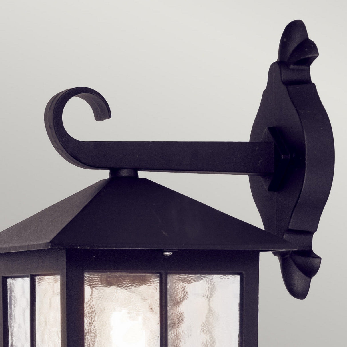 Close-up of the Winchester-1 1 Light Outdoor Wall Down Light - Black, highlighting its vintage-inspired black metal design with a curved arm and clear glass panes. This durable die-cast aluminum lantern is mounted on a decorative wall bracket against a light gray background.