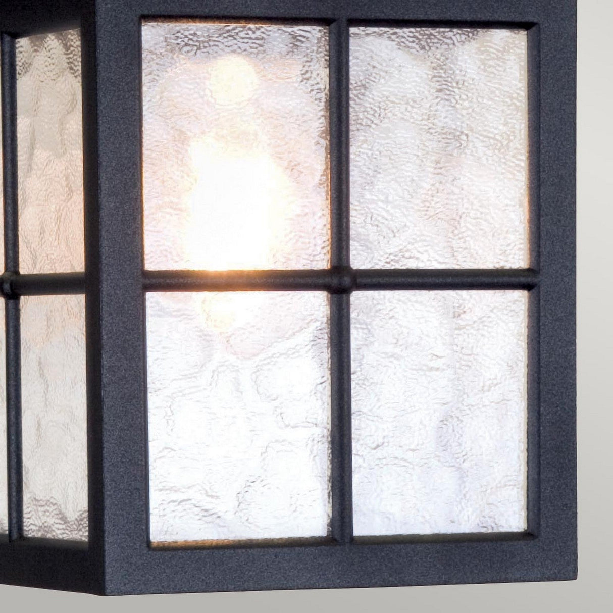 A close-up of the Winchester 1 Light Outdoor Chain Pendant - Black showcases its textured glass lantern and black metal frame, reminiscent of vintage outdoor lighting. The warm glow inside highlights the wavy patterns on the glass. Its classic rectangular design features a grid of six glass panes.