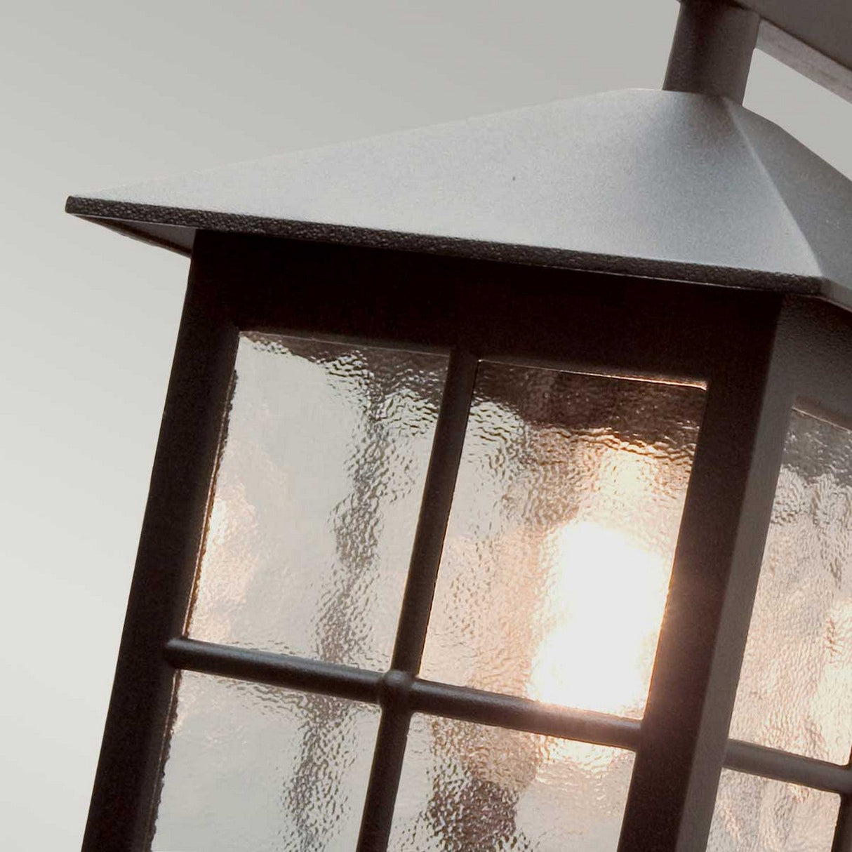 Close-up view of the Winchester-2 1 Light Outdoor Wall Down Light in black, featuring a lantern-style design made from die-cast aluminum. Its textured glass panels diffuse the warm glow, creating an inviting ambiance. The softly blurred background enhances this timeless outdoor wall lighting piece.