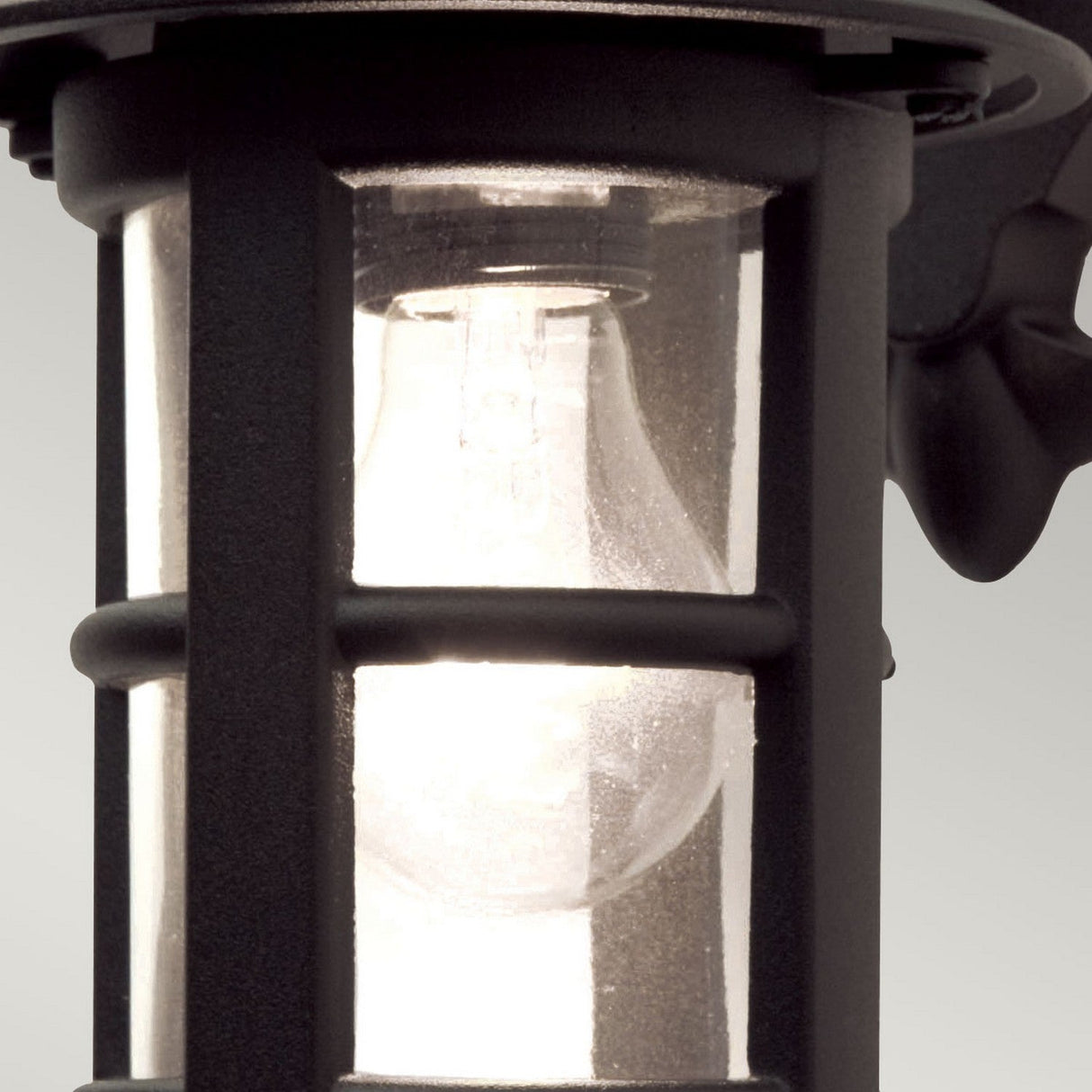 Close-up of the Hereford 1 Light Outdoor Wall Down Lantern - Black, showcasing its lantern-style design with a glowing bulb inside a clear glass casing. The piece is enveloped in a robust die-cast aluminium frame, bringing elegant charm to any exterior setting.