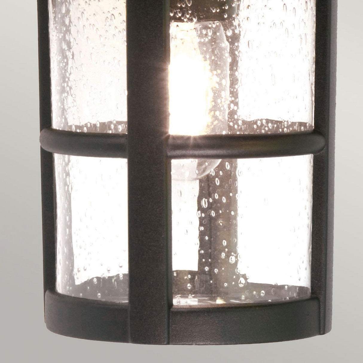 Close-up of the Hereford 1 Light Outdoor Large Wall Down Lantern in black, featuring a lit bulb inside. The bubbled texture of its cylindrical glass adds charm, while the black metal frame enhances its elegance.