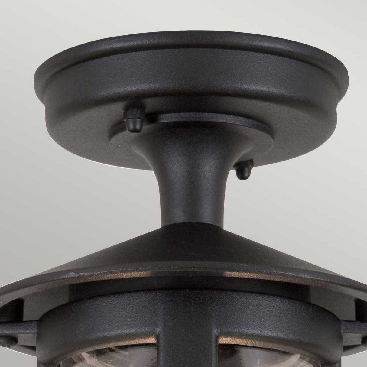 Close-up of the Hereford-2 1 Light Outdoor Porch Lantern - Black, featuring its black frame with a round base and a downward-facing lamp enclosed in clear glass panels. This traditional English lantern-style fixture is mounted on a pale green ceiling, enhancing your outdoor lighting setup with charm.