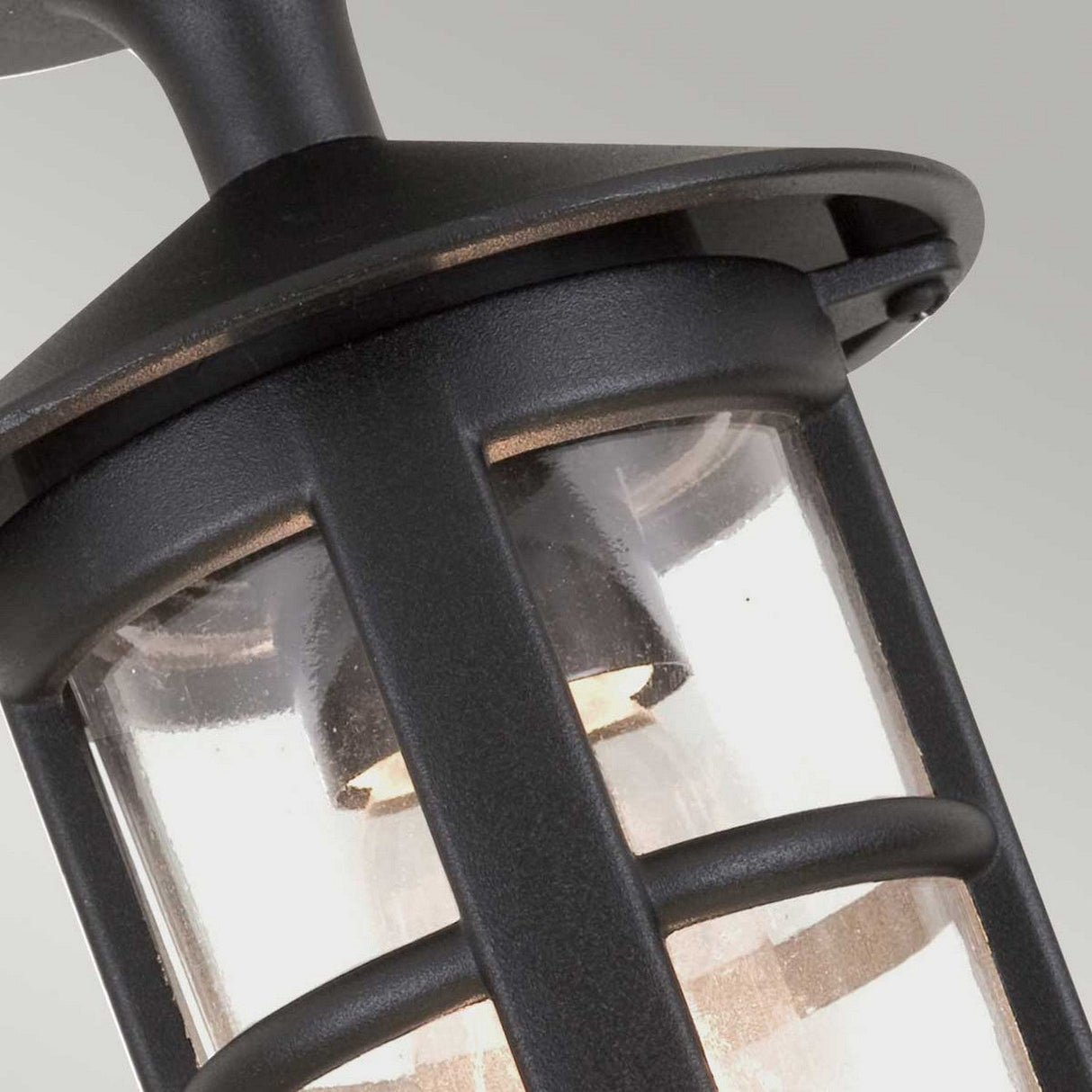 Close-up of the Hereford-2 1 Light Outdoor Porch Lantern - Black, an outdoor lighting fixture with a black metal frame and clear glass panels that showcases a light bulb inside. The design reflects a traditional English lantern style, featuring classic vertical and horizontal bars.