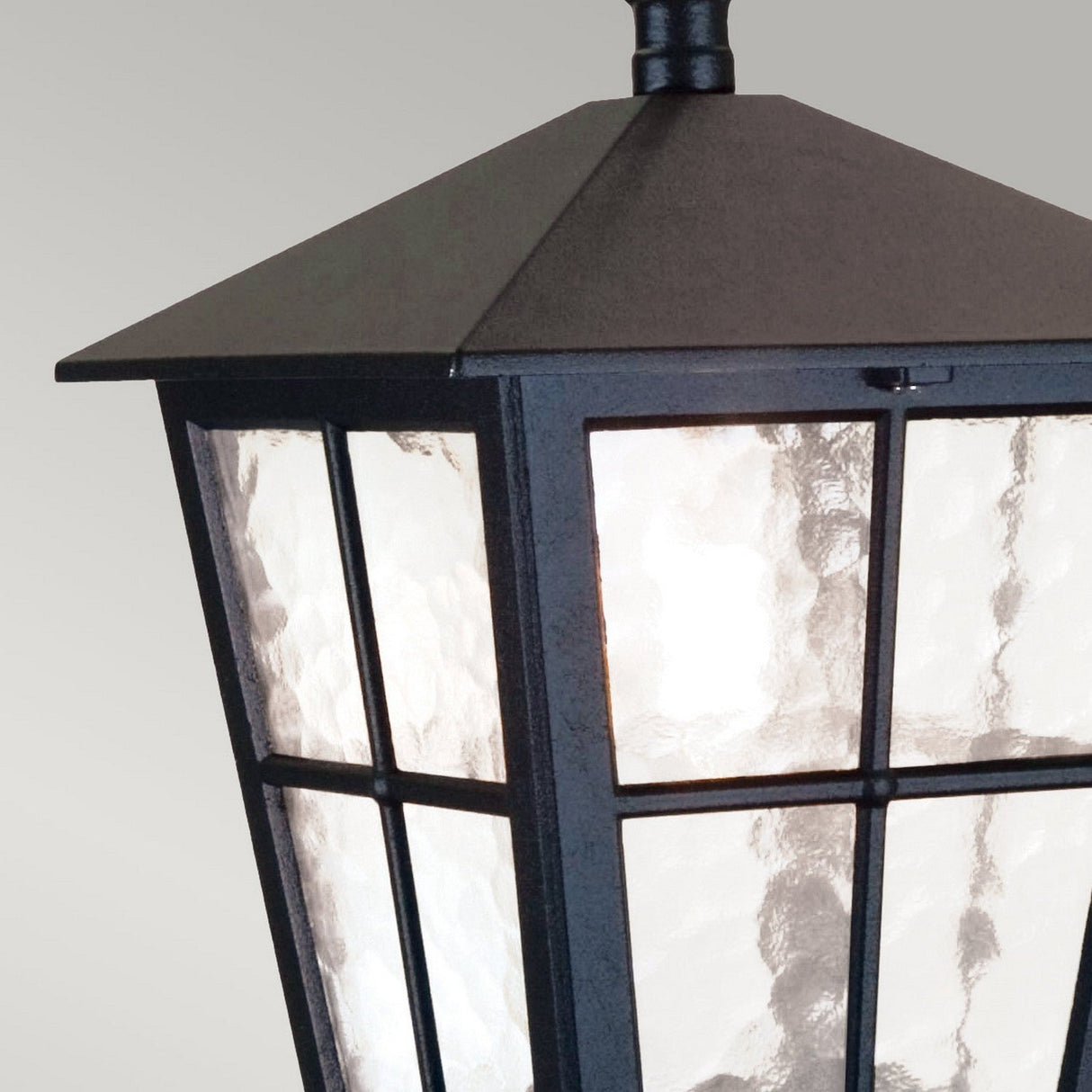 Close-up of a Canterbury 1 Light Outdoor Chain Pendant - Black, featuring a black lantern design with a sloped roof and frosted glass panels. The grid pattern on the glass lends it rustic charm, while the soft glow it emits is ideal for enhancing your exterior ambiance.