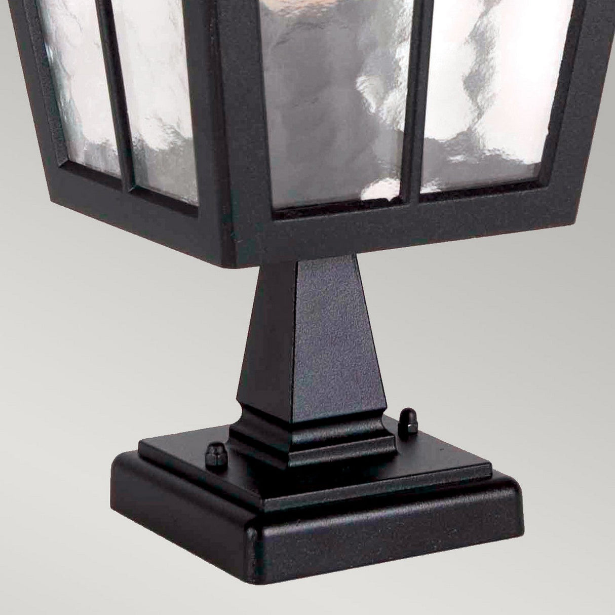 The Canterbury Outdoor Pedestal Lantern - Black showcases a sophisticated black finish with clear, textured glass panels, all mounted on a square base. Its sturdy construction and elegant design seamlessly enhance any neutral setting, capturing the essence of classic British style.