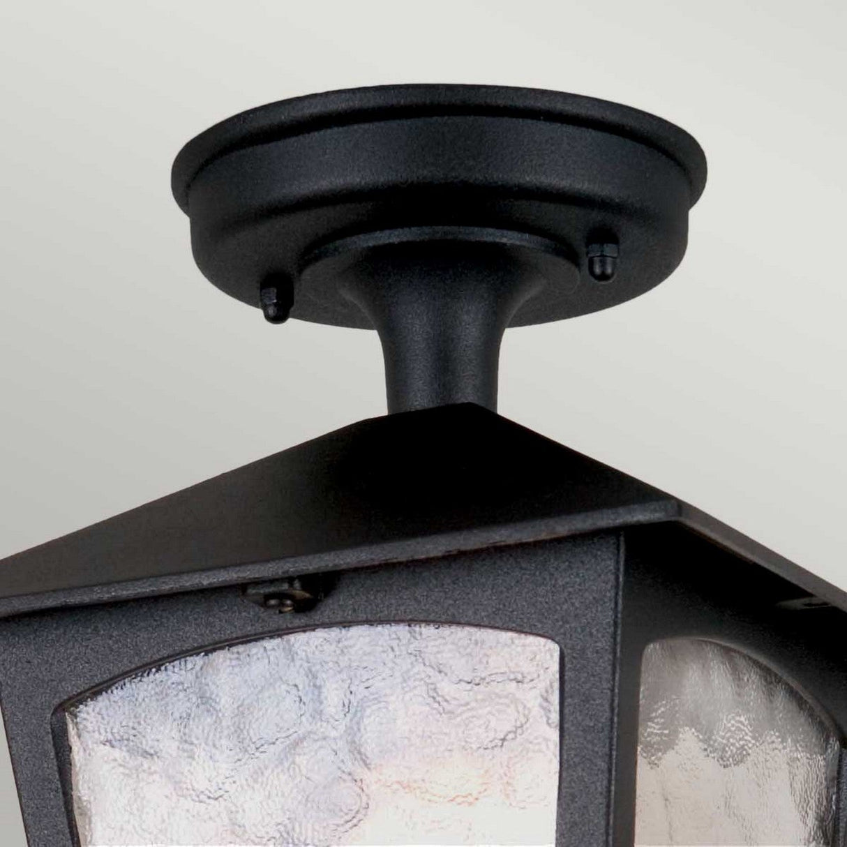 Close-up of the York 1 Light Outdoor Ceiling Light in black, featuring a square design crafted from durable die-cast aluminum. The fixture is mounted on a round base, combining simplicity and elegance. Its textured glass panel adds a vintage touch to the modern aesthetic.
