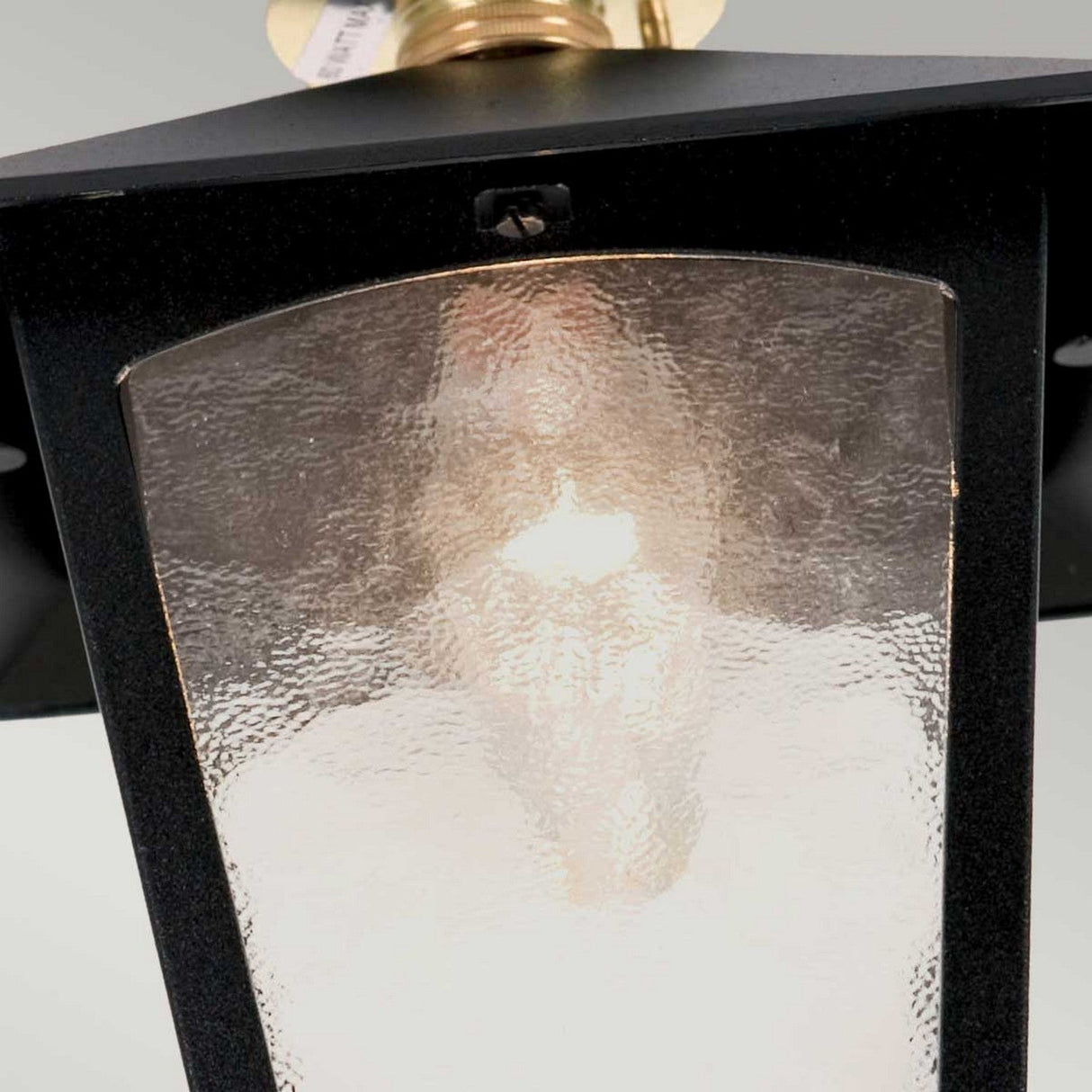 Close-up of the York 1 Light Outdoor Flush Porch Light in black, crafted from die-cast aluminum and featuring frosted glass, through which an E27 bulb emits a soft glow. The top and sides of the lantern are visible, with a partial view of the ceiling fixture.