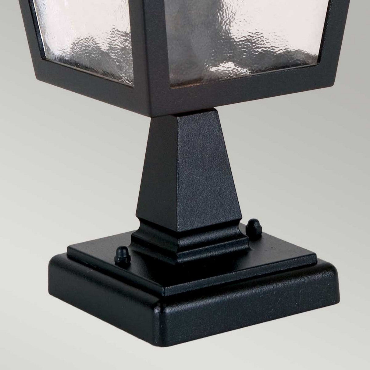 Close-up of the York 1 Light Pedestal Light - Black, crafted in die-cast aluminum for a vintage charm. Its pyramid-shaped base and frosted glass panels stand out against a plain, light gray background, adding elegance to any outdoor setting.