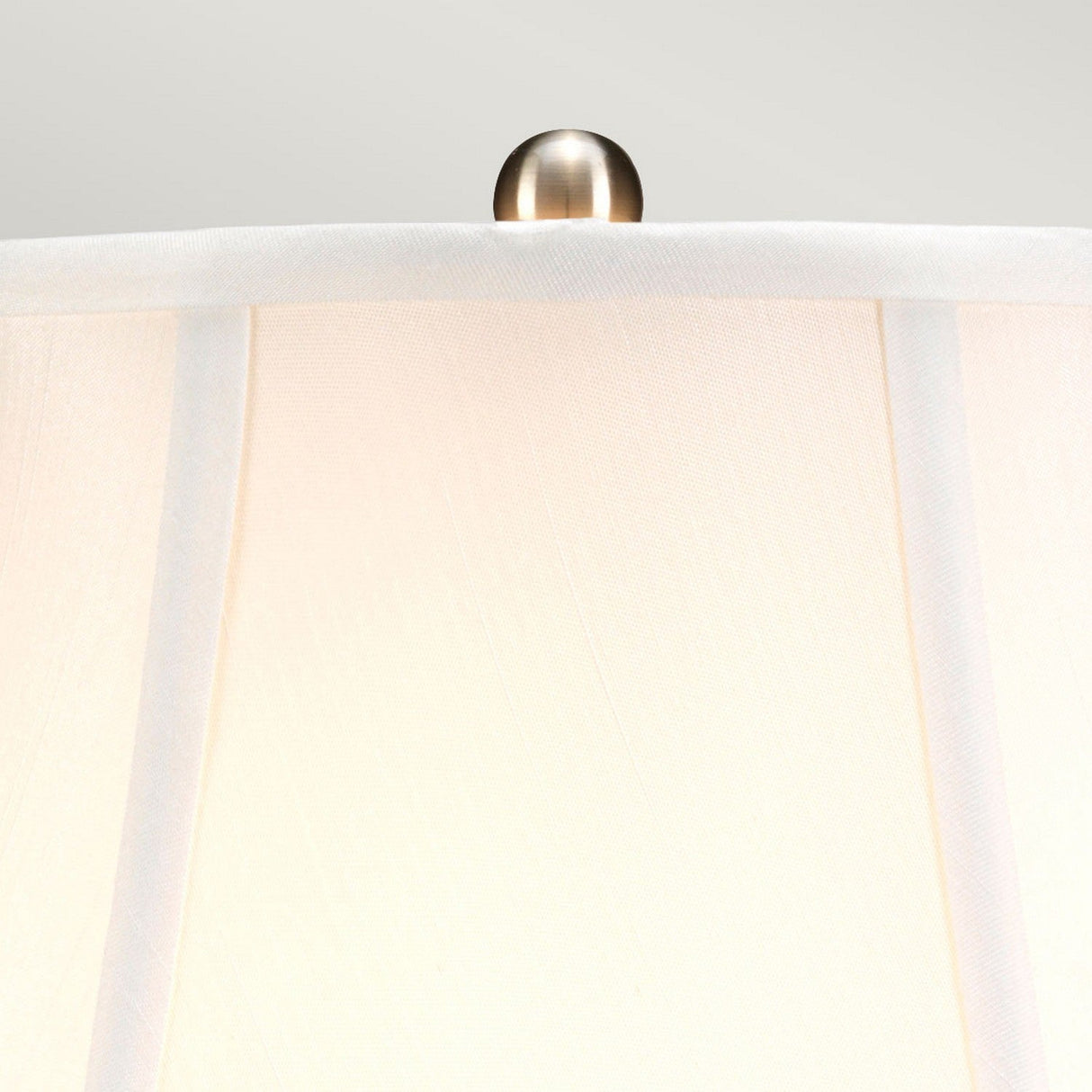 Close-up of the top part of a Blue Ginger Jar Table Lamp - Blue & White, featuring a white lampshade with a decorative metallic finial that echoes Chinese craftsmanship. The slightly pleated fabric is set against a neutral light background, enhancing the refined elegance often associated with porcelain table lamps.