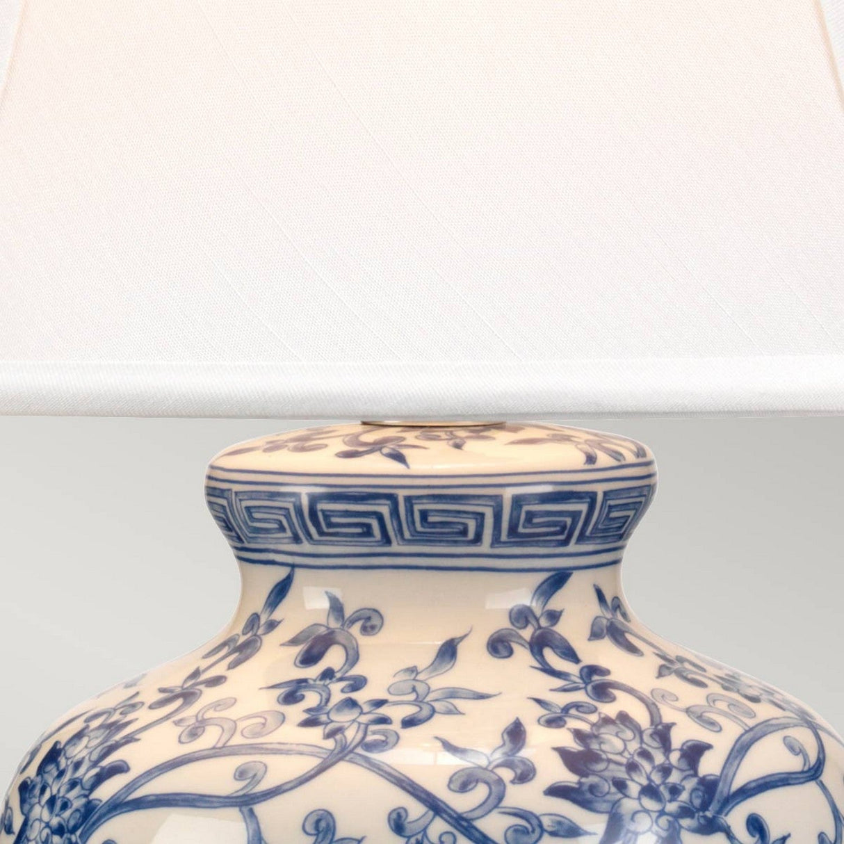 A close-up of the Blue Ginger Jar Table Lamp - Blue & White shows its ornate porcelain design, featuring intricate blue floral and geometric patterns on a white base. The plain white shade complements the detailed craftsmanship of the lamp's body, which highlights exquisite Chinese artistry.