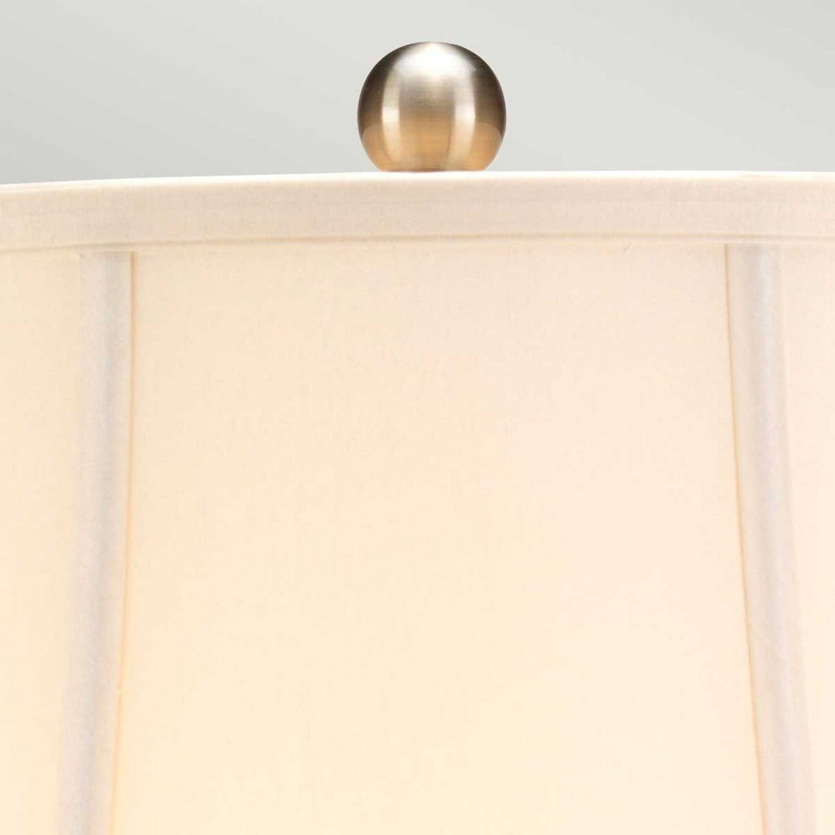 A close-up of the beige lampshade from the Blue Traditional Table Lamp - Blue & White, featuring a brushed metal finial at the top and set against a light gray background, evokes cultural charm reminiscent of Chinese porcelain artistry.