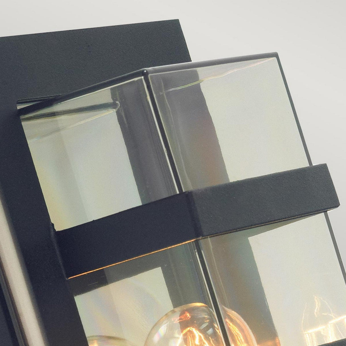 Close-up of the Boden Outdoor 1 Light Wall Light, showcasing its Art Deco design with clear glass panels and sleek black metal accents. The fixture's transparency reveals an exposed bulb, offering a touch of elegance to any exterior space.
