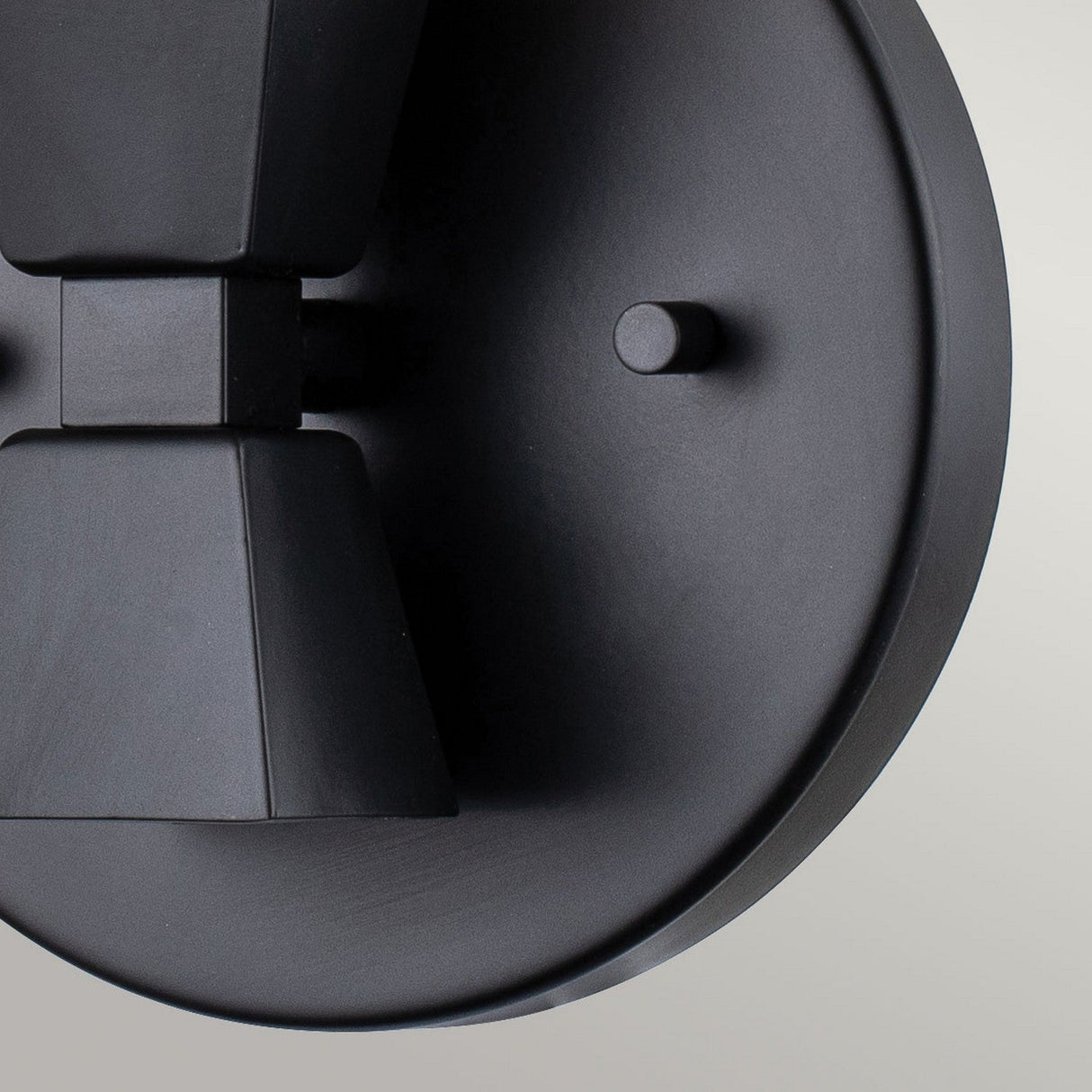 Close-up of the Bowtie 1 Light Wall Light in matte black against a light gray background. Its circular base and angular detailing craft a minimalist, geometric aesthetic, ideal for modern bathroom lighting schemes.