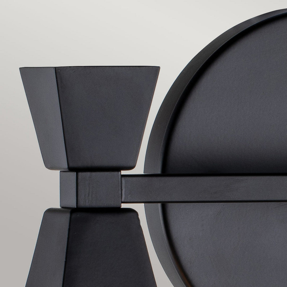 Close-up of a Bowtie 2 Light Wall Light in matte black, showcasing its geometric design. It features clean lines and a matte finish, reminiscent of contemporary candle holders, set against a neutral background, emphasizing its minimalist style.