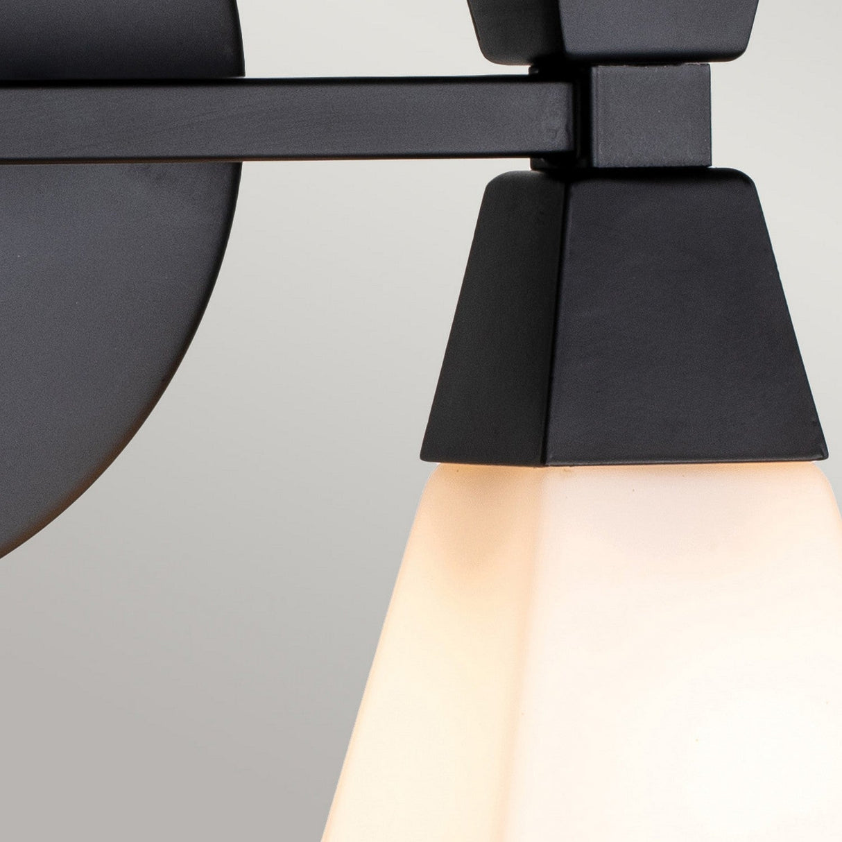 Close-up of the Bowtie 2 Light Wall Light in matte black, showcasing its metal frame with opal glass shades. The light is ideal for bathroom lighting and is turned on, casting a soft glow against a neutral background.