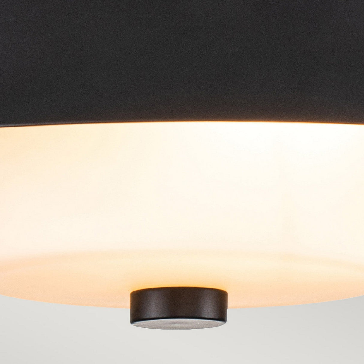 Here's a close-up of the Bowtie 2 Light Flush in matte black. It features a glowing white opal glass interior and has a round base with a small black circular piece at the center, providing soft, warm illumination. The modern design looks perfect against a neutral background, making it ideal for any contemporary space.