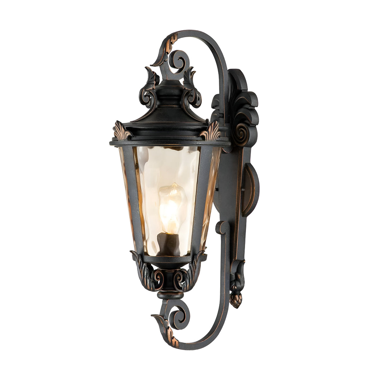 The Baltimore 1 Light Outdoor Large Wall Lantern features a weathered bronze finish and decorative scrollwork. It contains a single illuminated bulb inside an amber-tinted glass enclosure, casting a warm glow over your outdoor space.