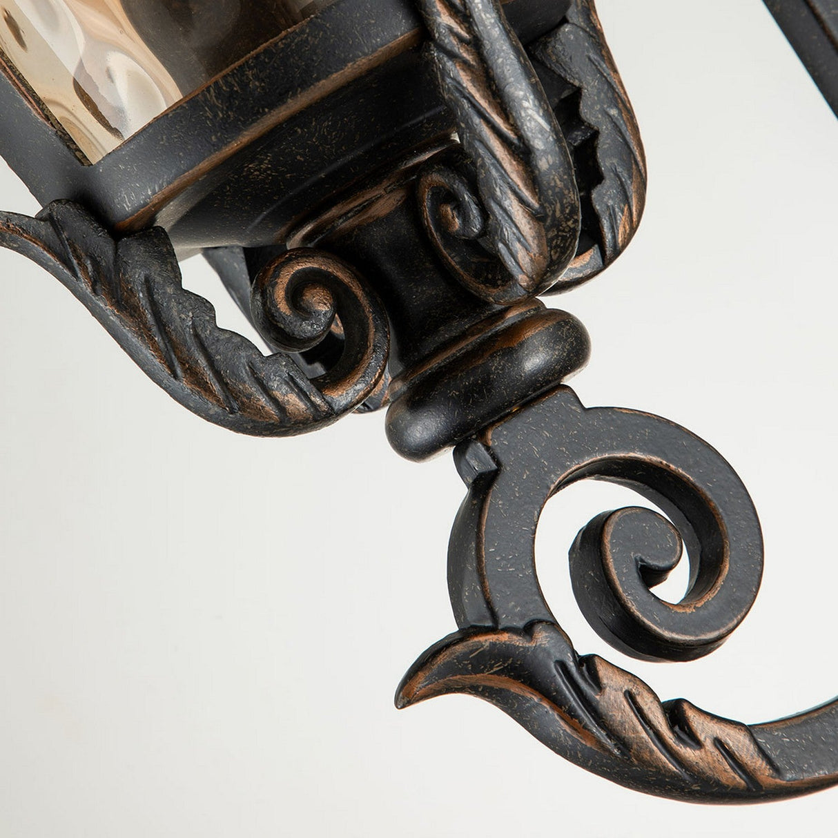 This is a close-up of the Baltimore 1 Light Outdoor Medium Wall Lantern in a weathered bronze finish. The vintage-inspired design boasts intricate scrollwork detail, leaf-like accents, and a textured glass panel that together create an elegant and classic appearance.