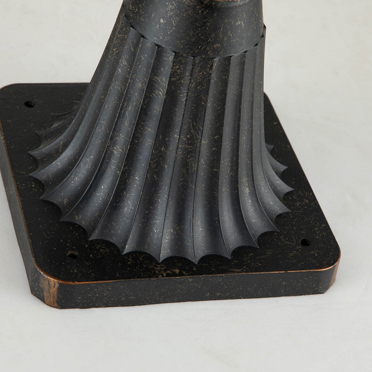 Close-up of the Baltimore 1 Light Medium Pedestal Lantern, showcasing its decorative, antique-style metal base with a fluted design and square bottom. Featuring a weathered bronze finish, it is perfect for an outdoor setting and boasts an elegant texture on a light backdrop.