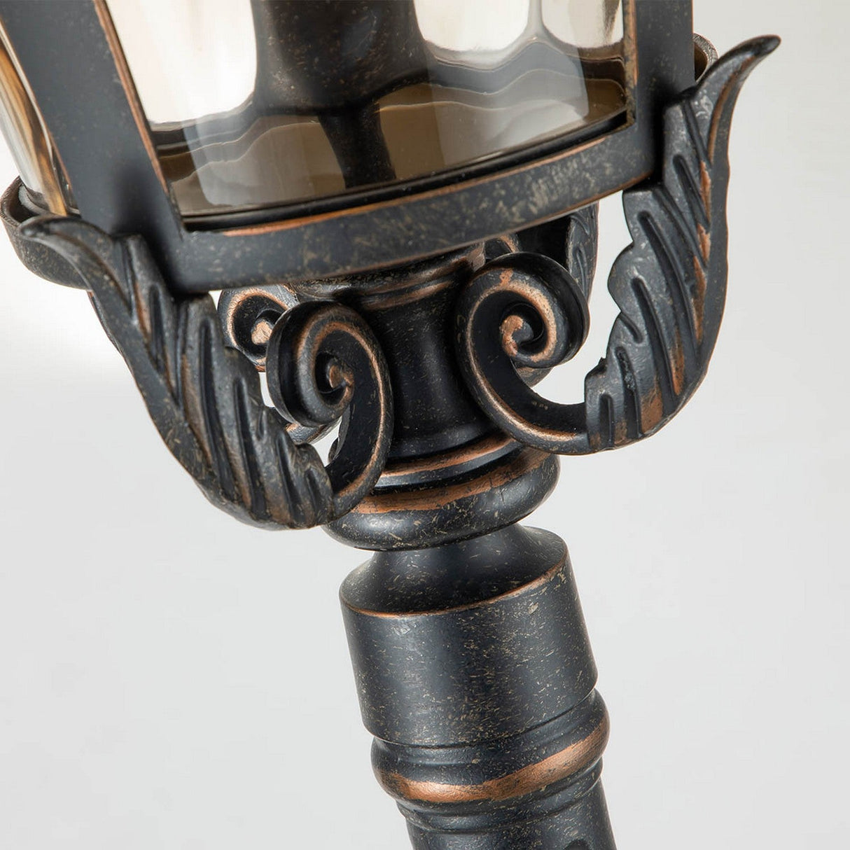 Close-up of the Baltimore 1 Light Medium Pillar, an outdoor lamp post with a vintage aesthetic. This lighting design boasts ornate scrolling details and a weathered bronze finish, exuding an elegant and classic style.