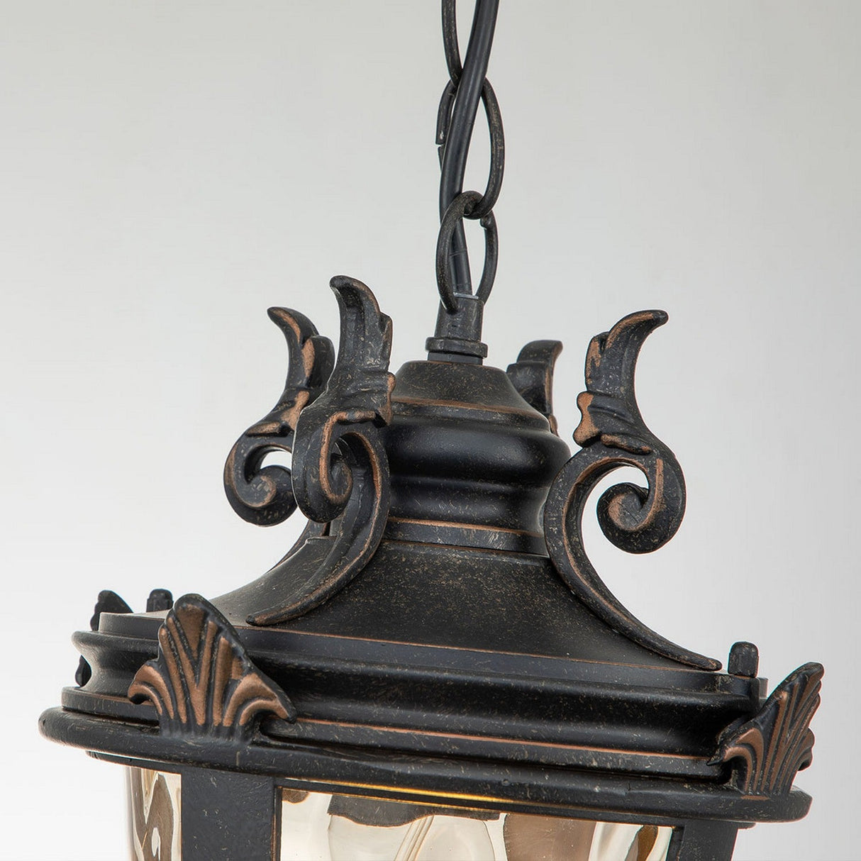 A detailed view of the Baltimore 1 Light Outdoor Medium Chain Pendant reveals an ornate black lantern adorned with intricate scrollwork and decorative metal designs. This piece exudes a classic, vintage charm with its weathered bronze finish.