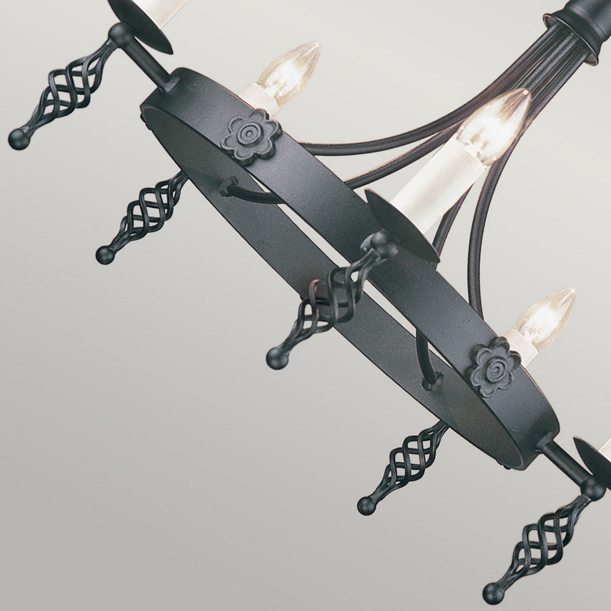 A detailed look at the Belfry 5 Light Chandelier - Black reveals its hand-crafted design with black wrought iron, featuring vintage-style bulbs and ornate, twisted metal arms on a white background, capturing the essence of traditional artistry.
