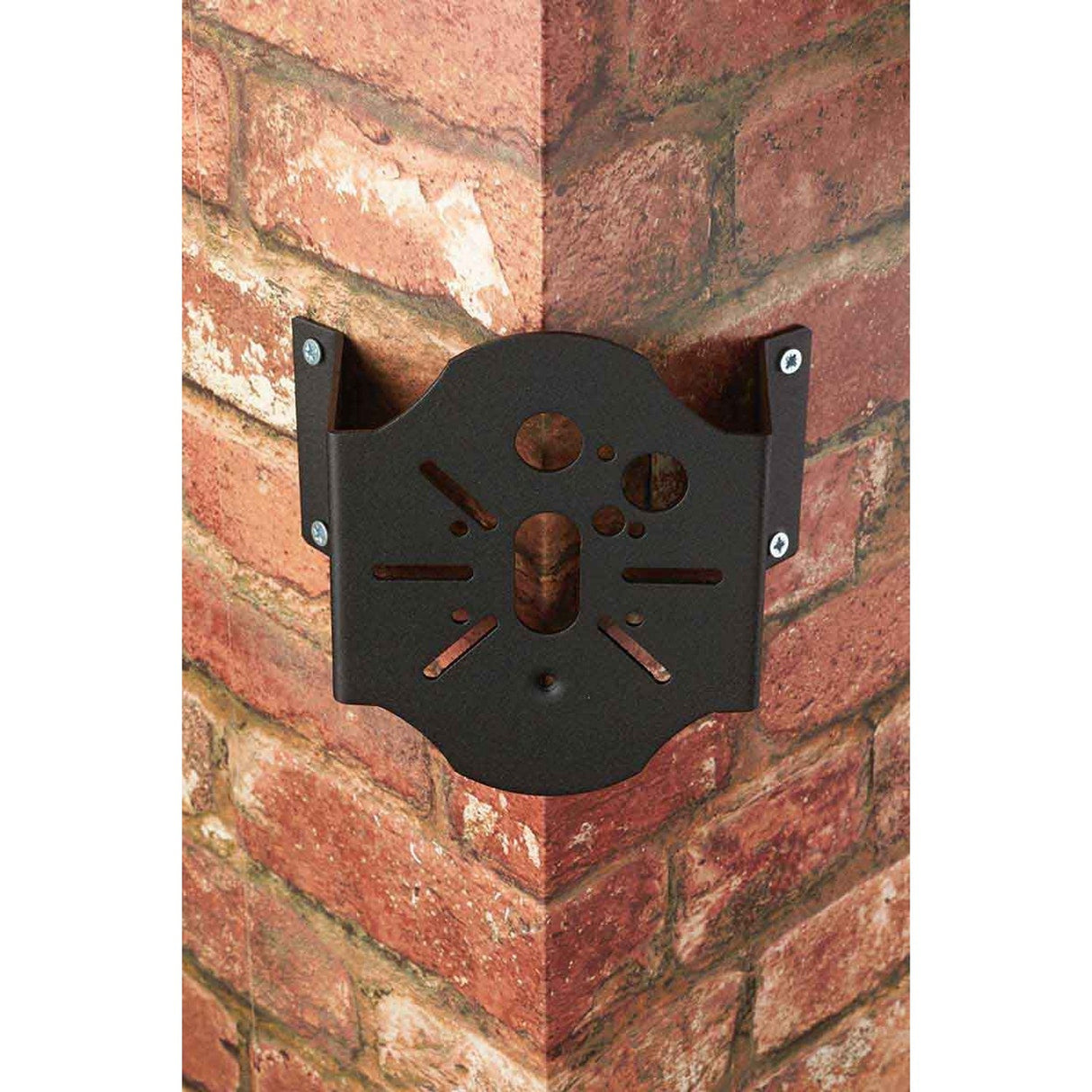 The Corner-2 Bracket - Black is a metal corner bracket attached to a red brick corner, making it perfect for outdoor use in securing devices or objects. It includes various holes and cutouts and is secured with four visible screws.