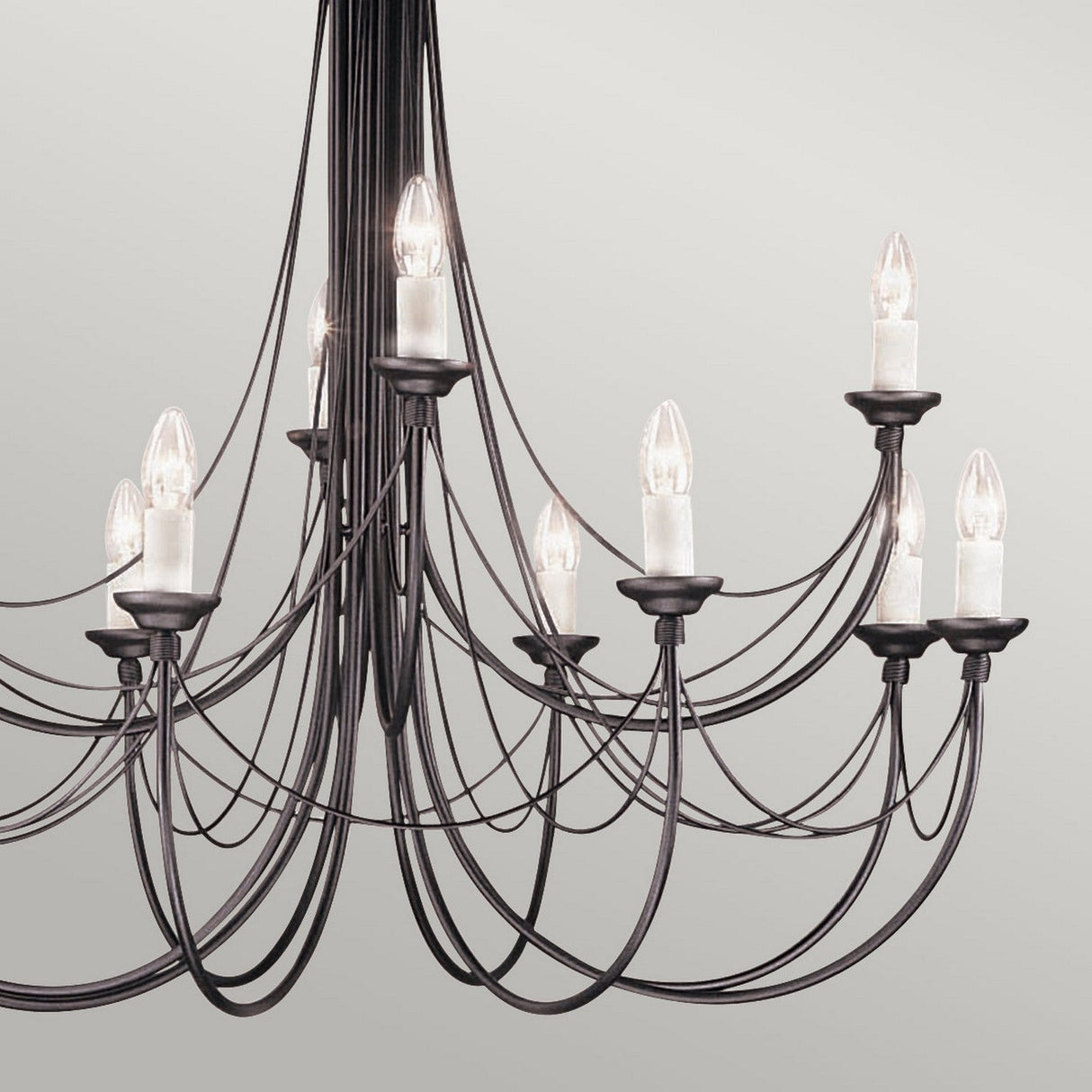 The Carisbrooke 12 Light Chandelier in black features an elegant Gothic design, with multiple curved arms, each supporting a candle-shaped bulb. Suspended against a plain, light gray background, this traditional chandelier exudes a sophisticated and classic appearance.