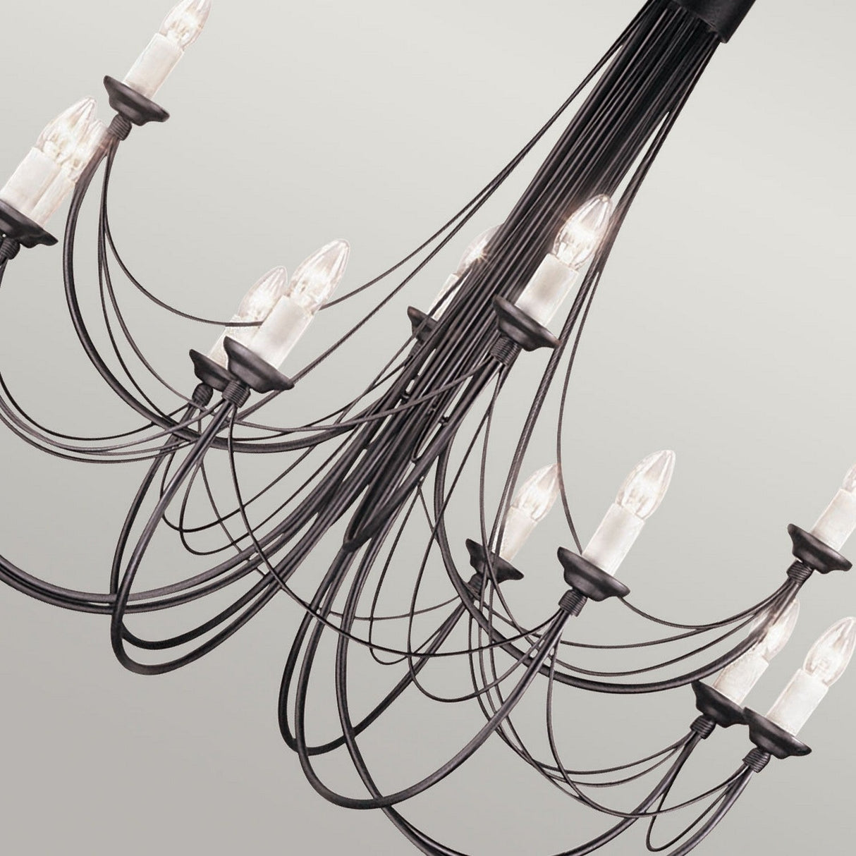 The Carisbrooke 12 Light Chandelier in Black boasts a modern design with numerous delicate wires extending to small, exposed light bulbs. Its minimalist aesthetic exudes a touch of Gothic elegance against a plain light gray background.